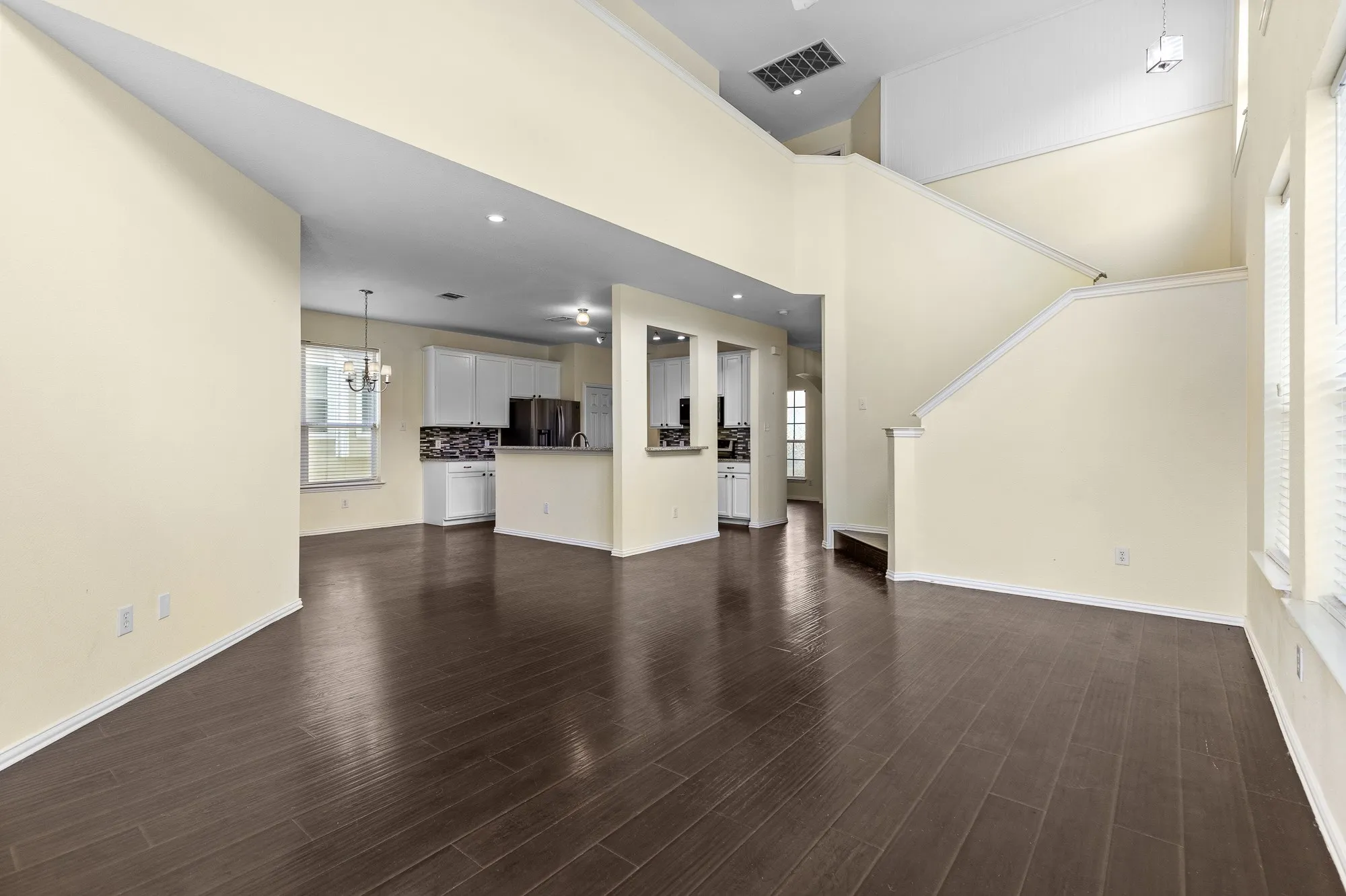 Spacious living area featuring high ceilings, dark wood-finish flooring, and multiple windows with blinds