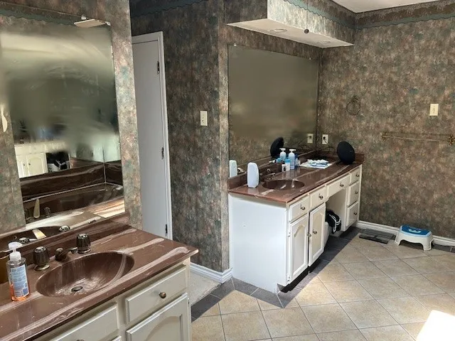 Spacious bathroom featuring dual vanities with integrated sinks, ample counter space, and decorative wall coverings