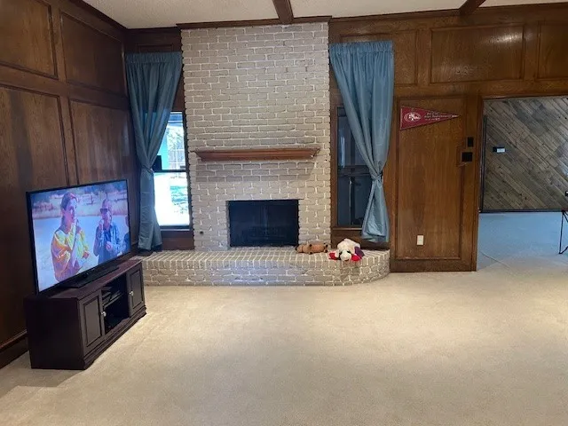 Living space featuring a brick fireplace with a wood mantle, wood paneling, and exposed ceiling beams