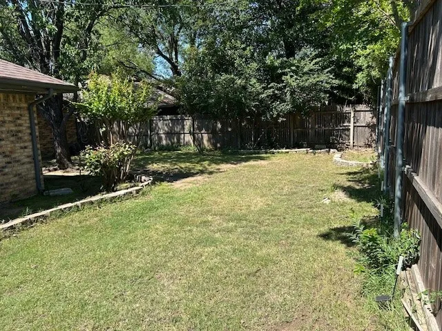 Expansive backyard featuring a green lawn, mature trees, and a perimeter wooden fence