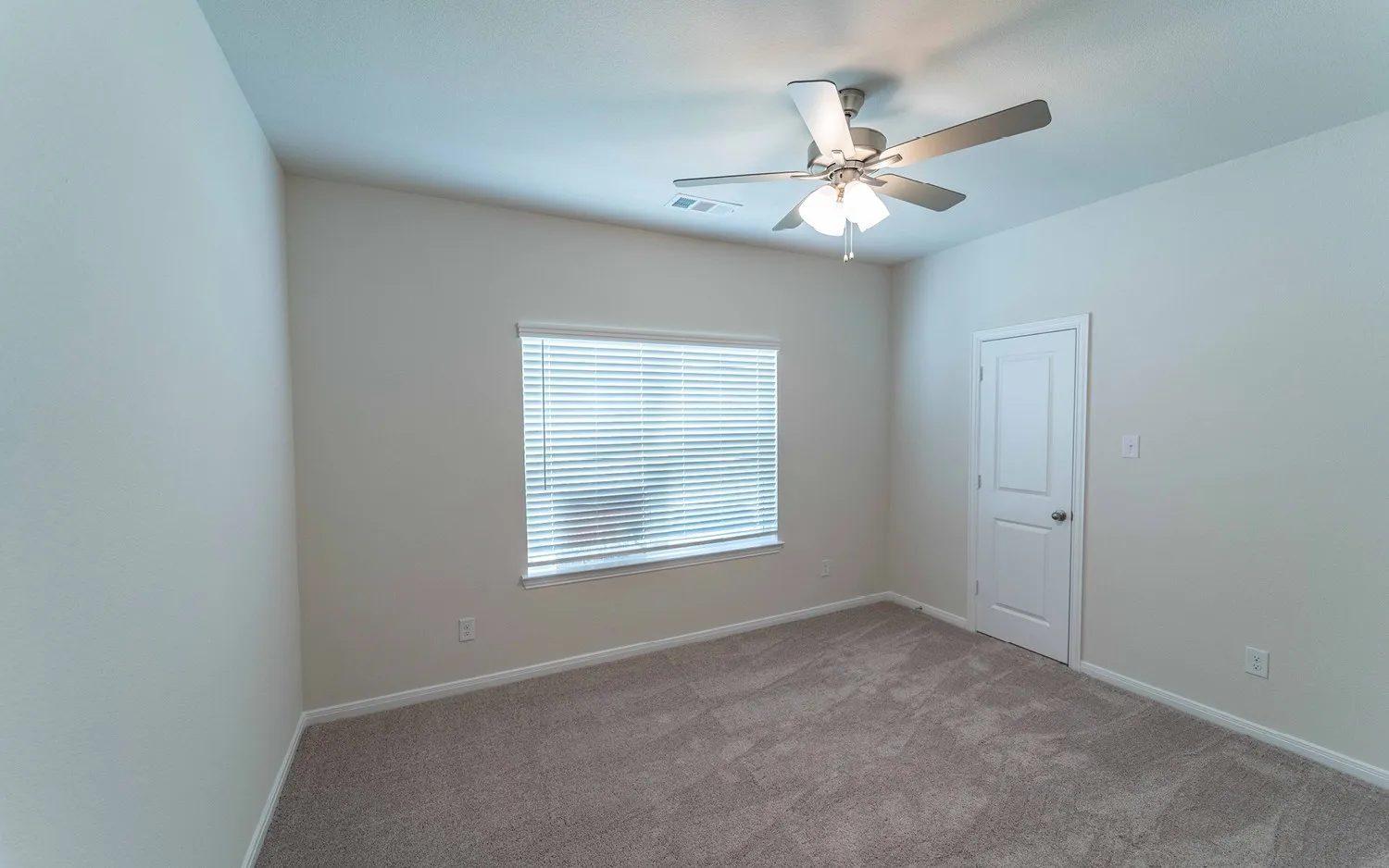 Carpeted room featuring neutral-toned walls, a window with blinds, a white paneled door, and a ceiling fan with integrated lighting