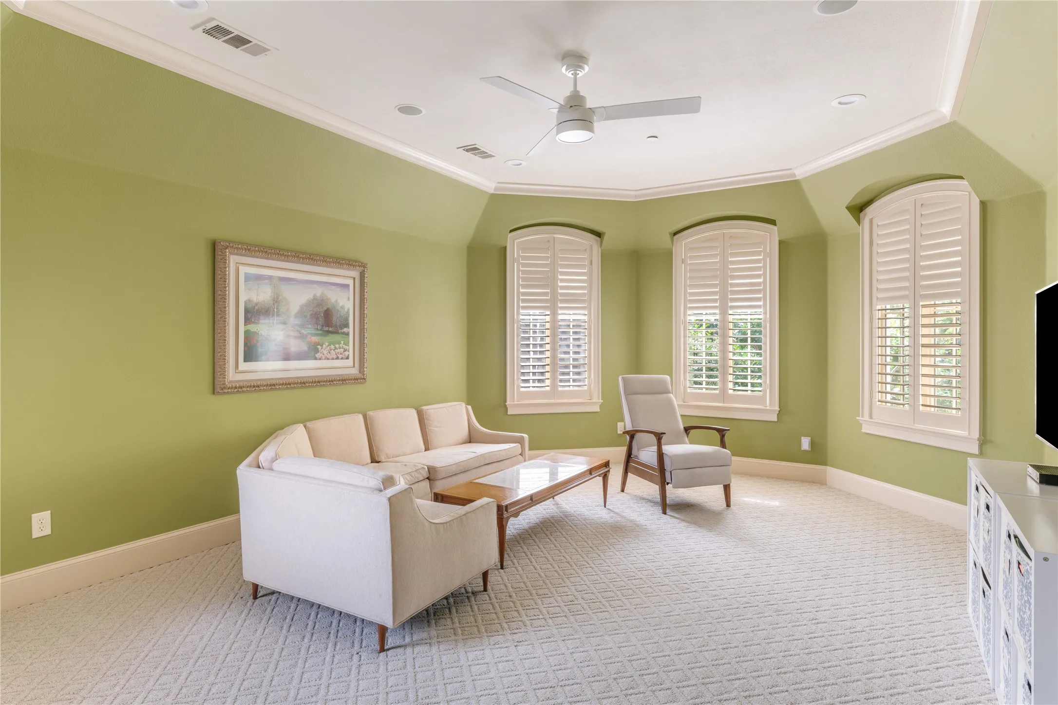 Carpeted room featuring three arched windows with plantation shutters, a vaulted ceiling with crown molding, a ceiling fan, and recessed lighting