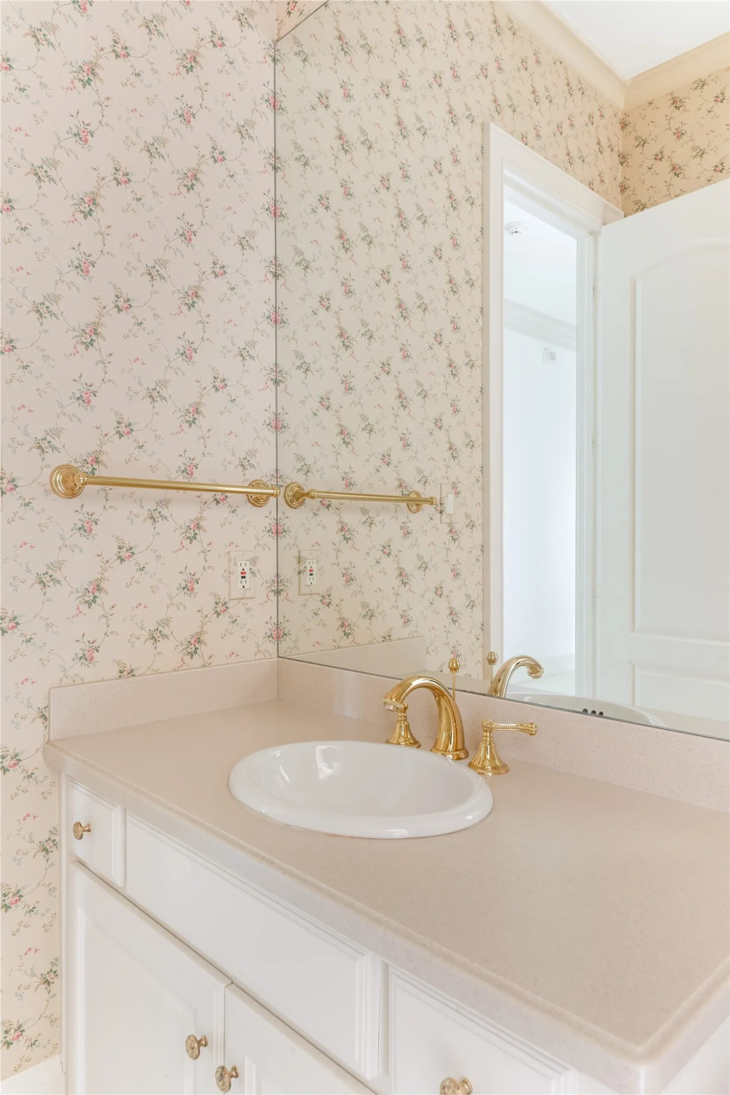 Bathroom vanity featuring a white oval undermount sink, brass-finish faucet, and a light-toned countertop