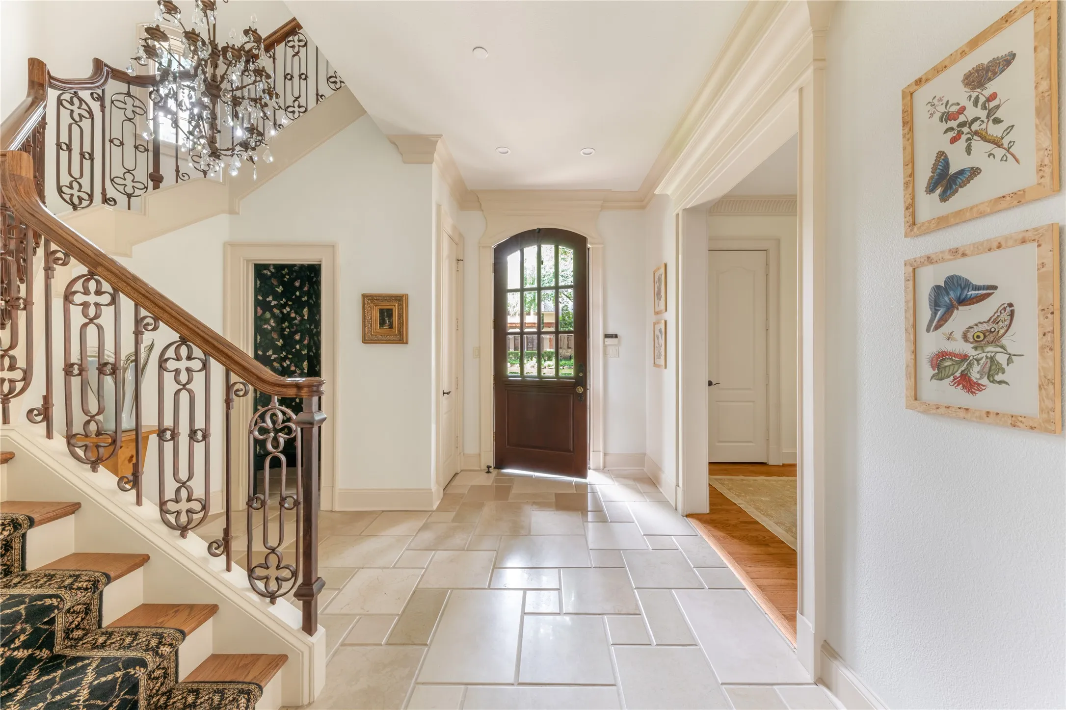 Gracious entryway featuring a custom wrought iron and wood banister, a multi-tiered crystal chandelier, and a dark wood arched door with glass panels
