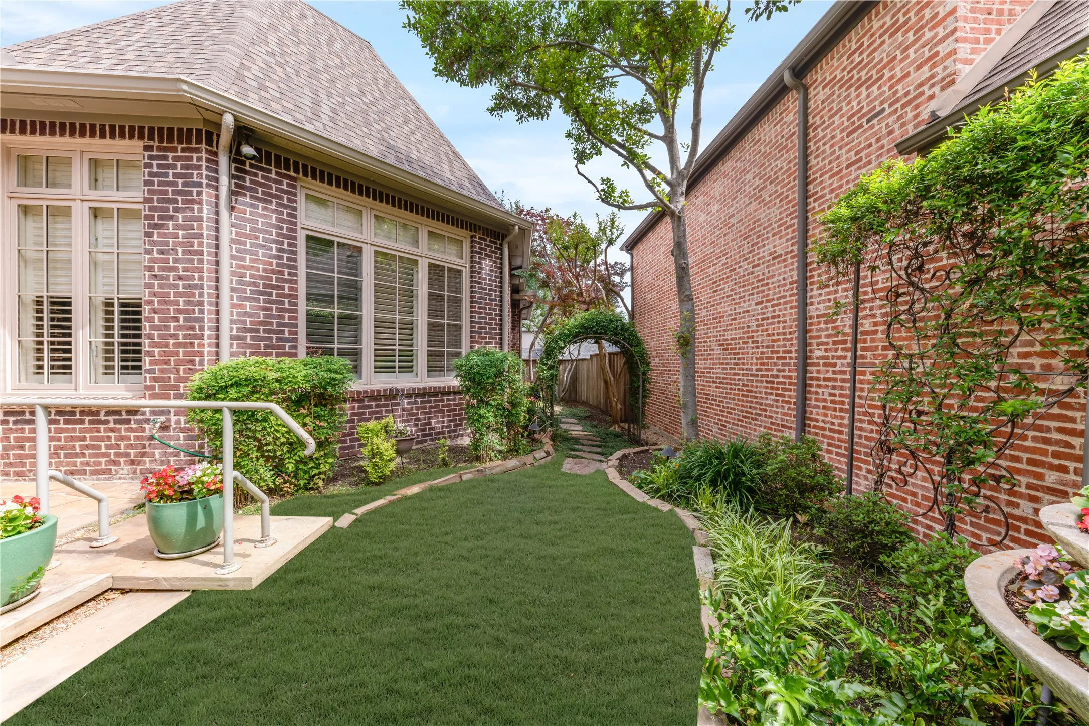 Side yard featuring a lush lawn, mature landscaping, and a brick exterior viewed from multiple windows