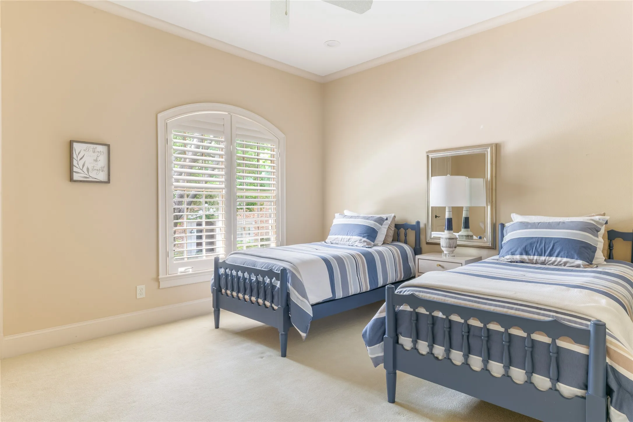 Upstairs secondary bedroom featuring an arched window with white plantation shutters, crown molding