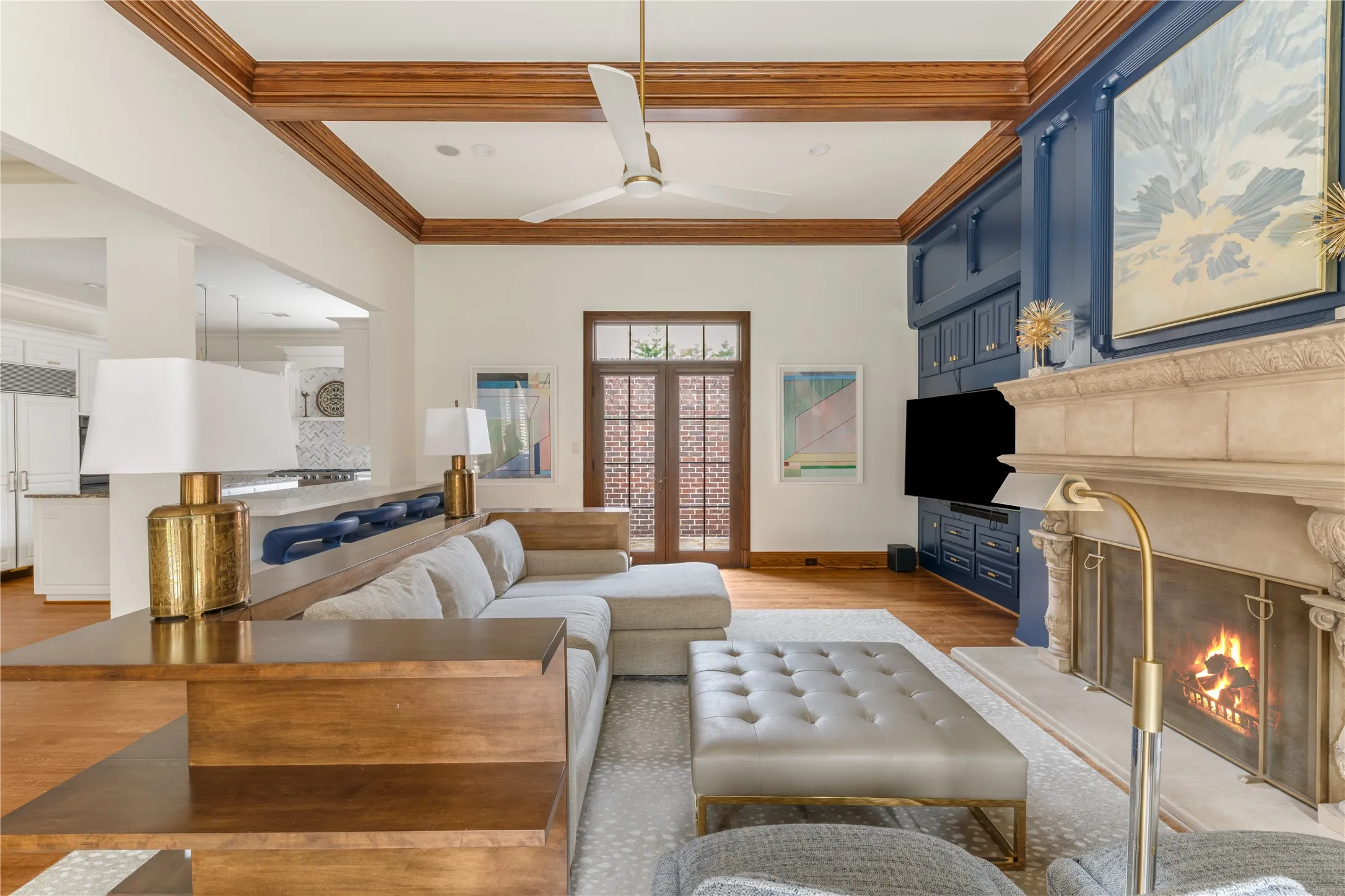 Living area featuring a stone fireplace with decorative mantel, extensive built-in cabinetry, wood-finish flooring, and a coffered ceiling with wood beams