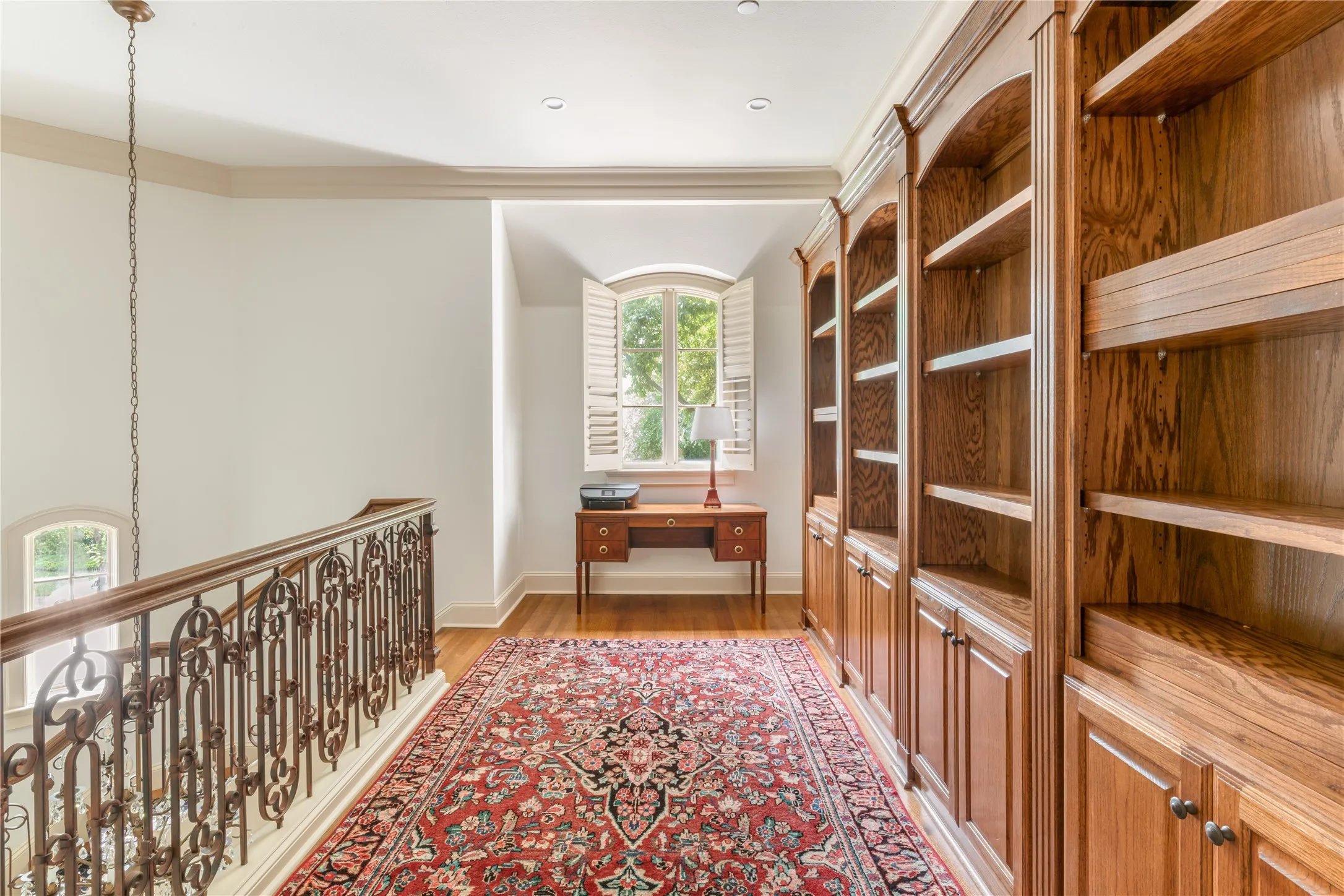 Hallway featuring extensive built-in wood cabinetry with integrated shelving and storage, wood-finish flooring, and an ornate wrought-iron stair railing