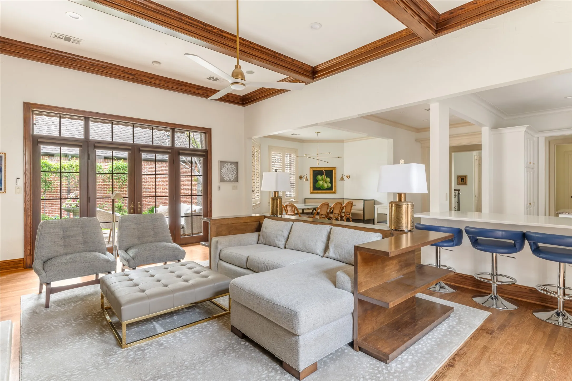 Coffered ceilings accent a living area featuring wood-finish flooring and extensive glass panel doors