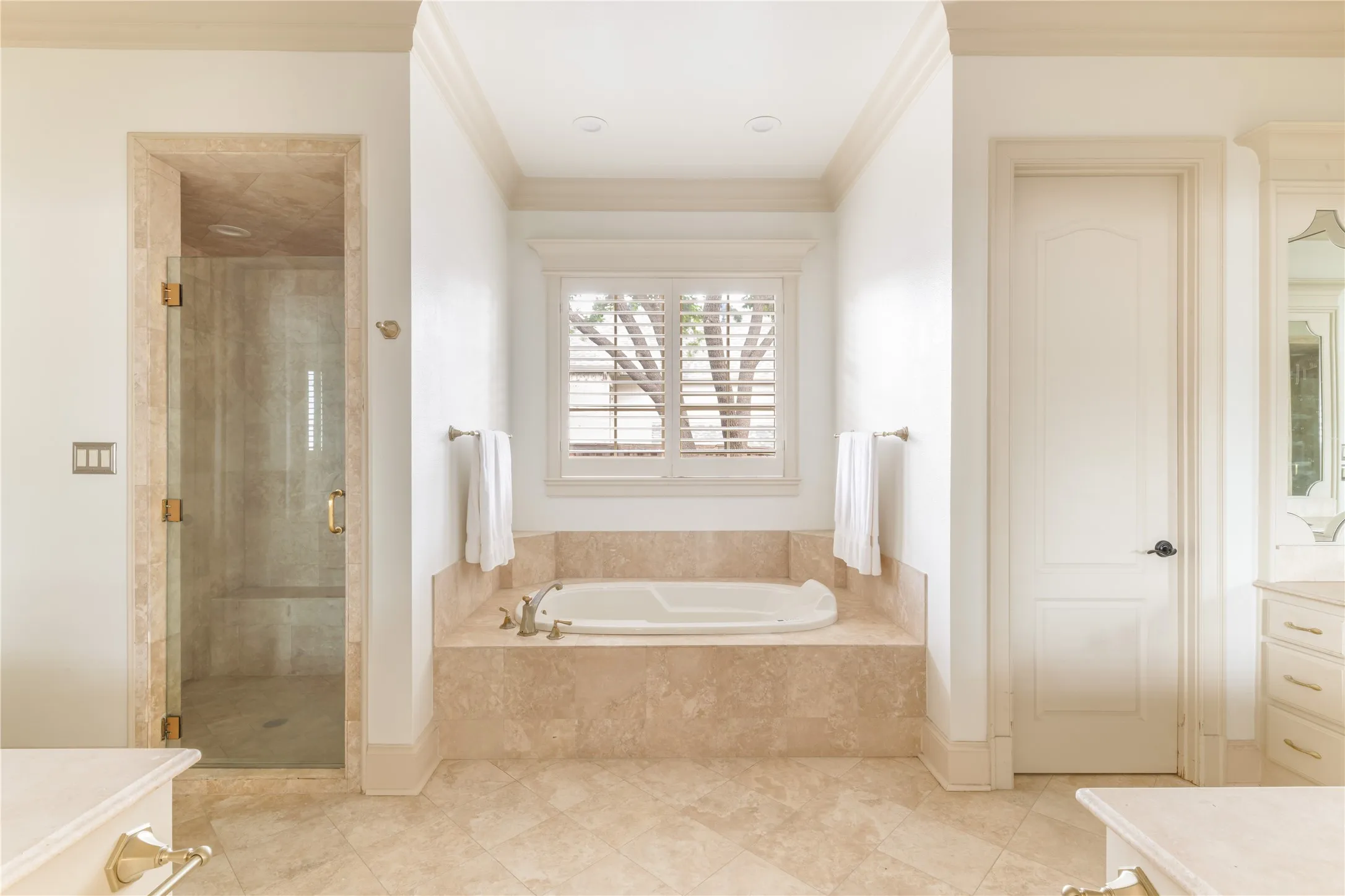 Spacious bathroom featuring a soaking tub with stone surround, a separate glass-enclosed shower with stone tiling, and plantation shutters