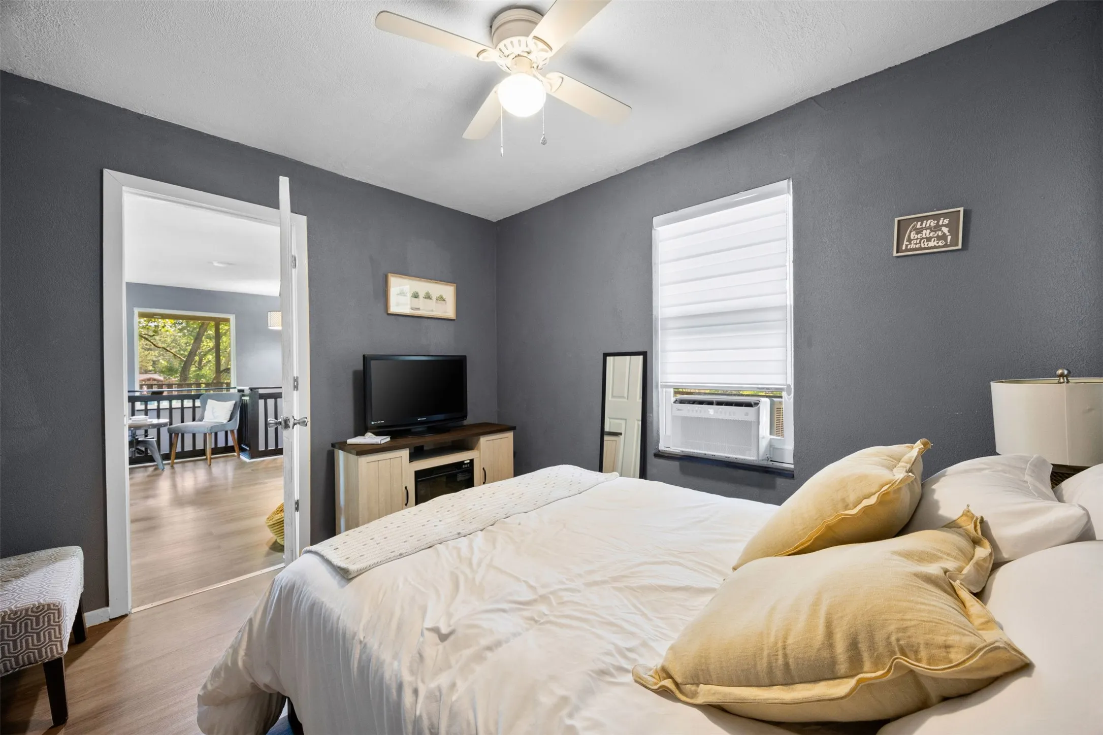 Bedroom featuring wood-finish flooring, a ceiling fan with integrated lighting, a window with horizontal blinds, and direct access to an outdoor deck area