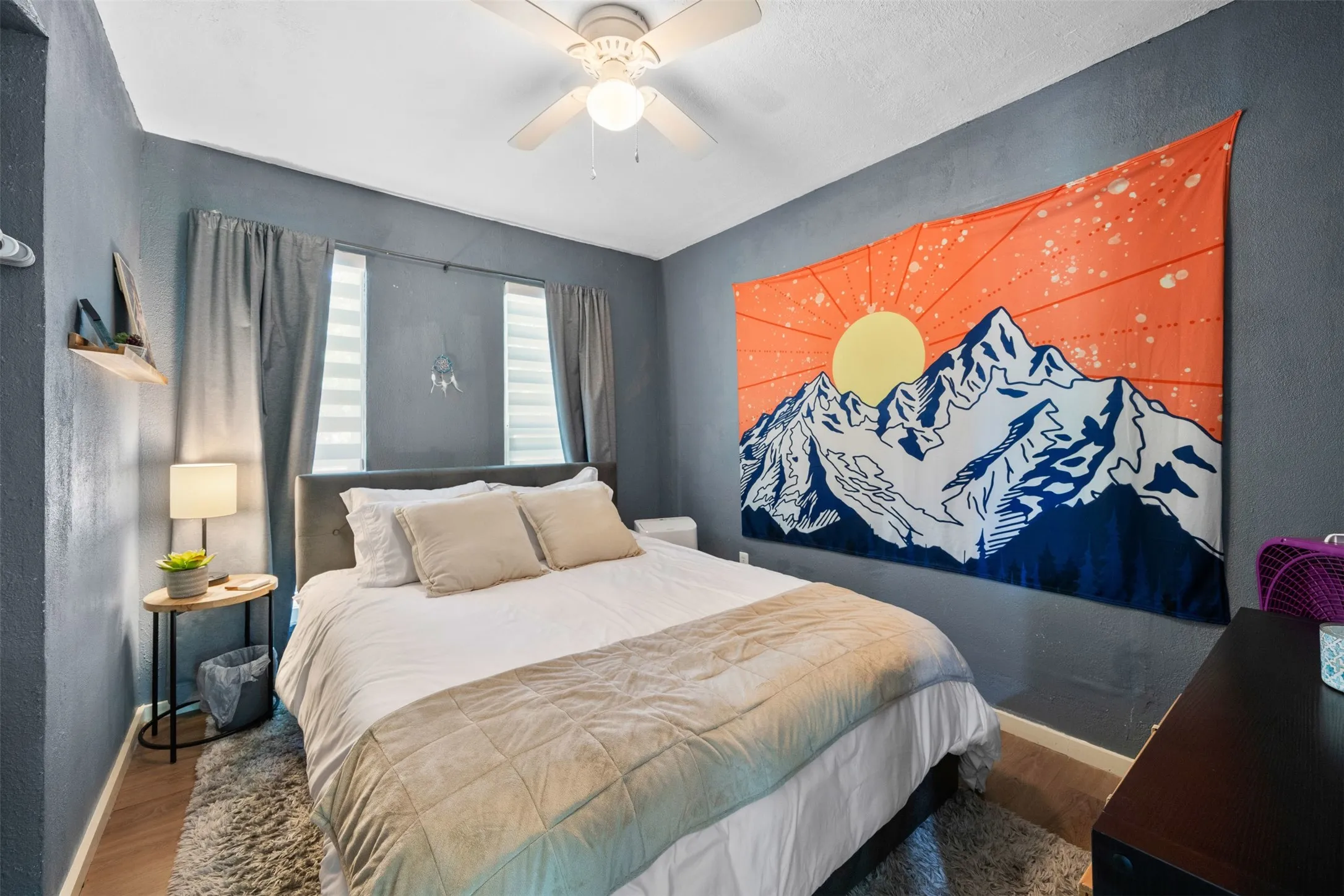 Bedroom featuring a ceiling fan, two windows with blinds and drapes, and wood-finish flooring