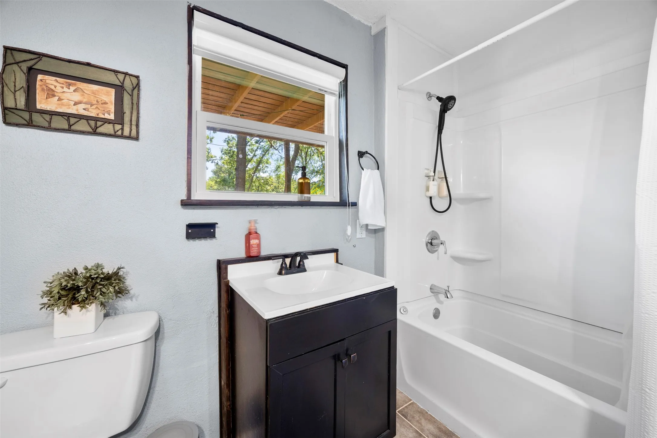 Bathroom featuring a white bathtub and shower surround, a dark wood-finish vanity with an integrated sink, and wood-finish flooring