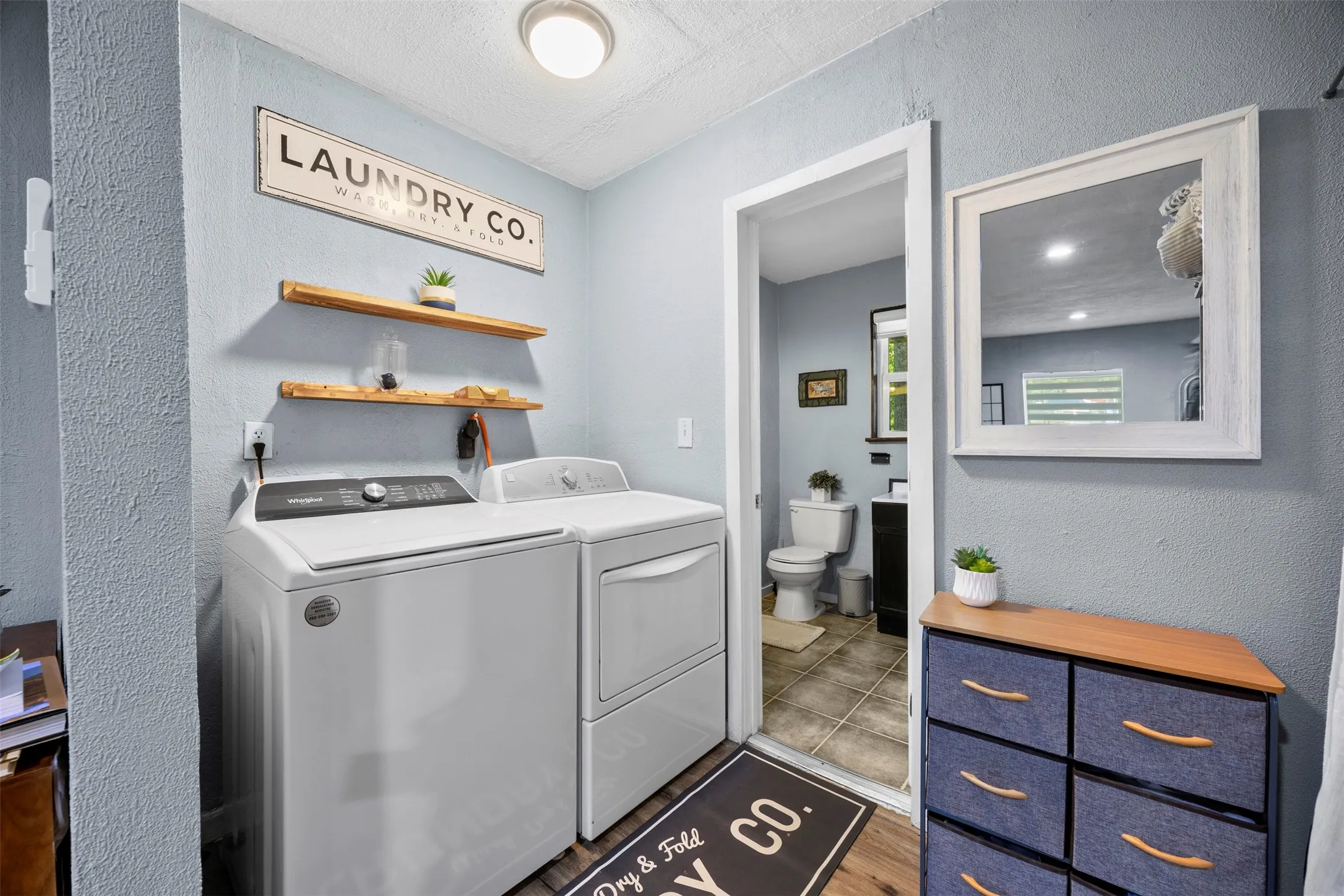 Dedicated laundry area featuring wood-finish flooring and two floating wood shelves