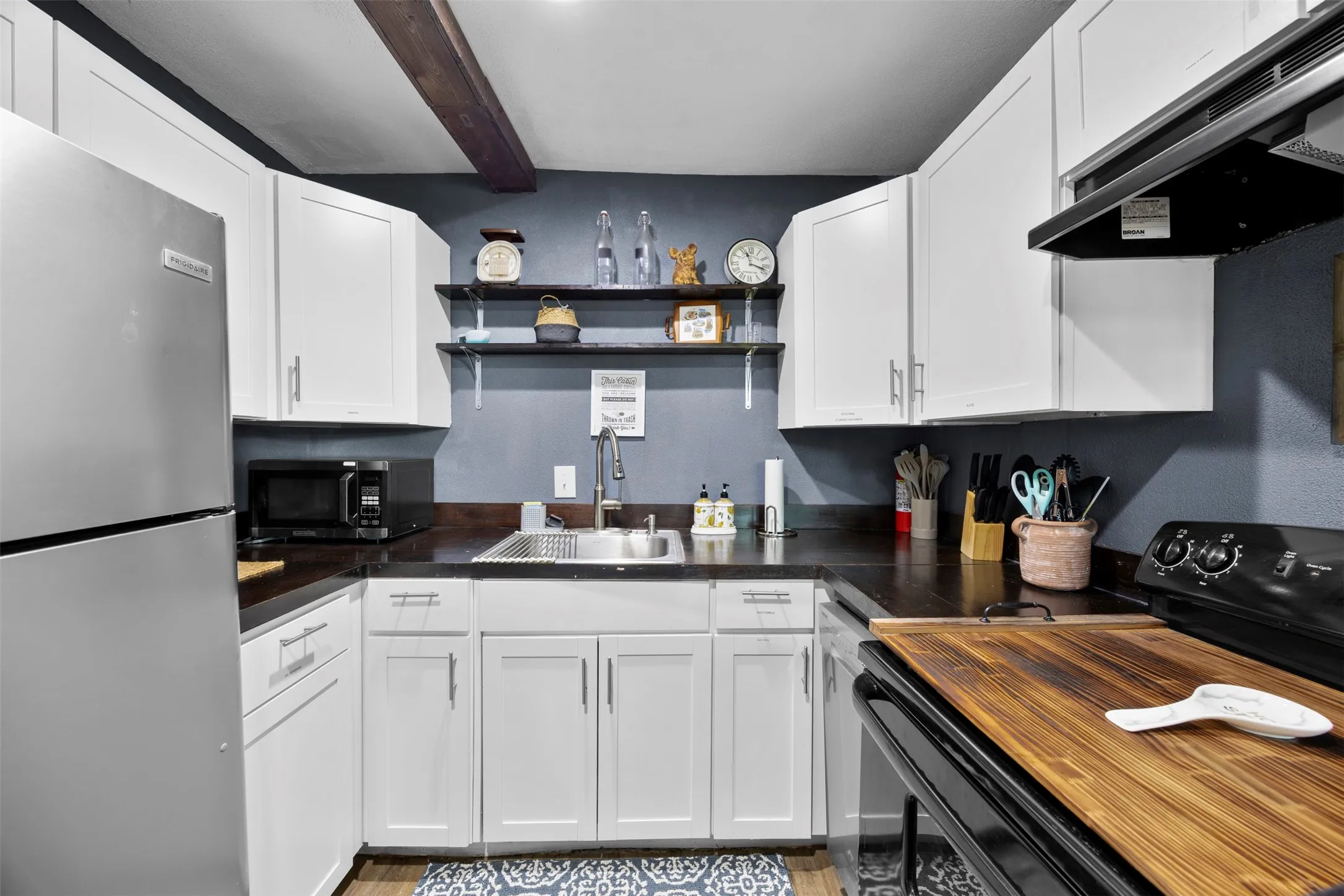 Compact kitchen featuring white shaker cabinetry, dark countertops, a stainless steel refrigerator, and wood-finish flooring