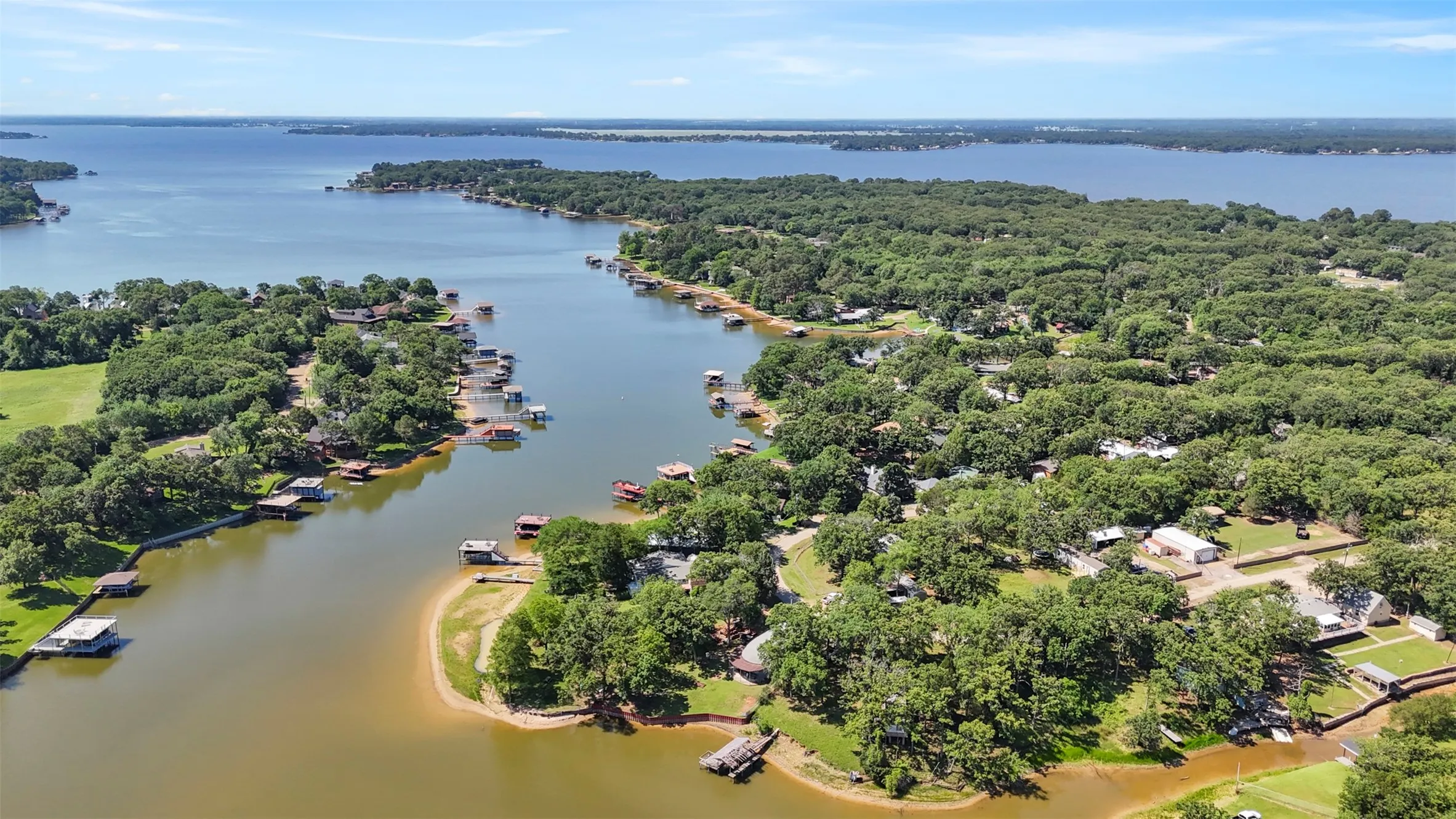 Expansive body of water with a narrow channel, surrounded by lush green trees and residential properties