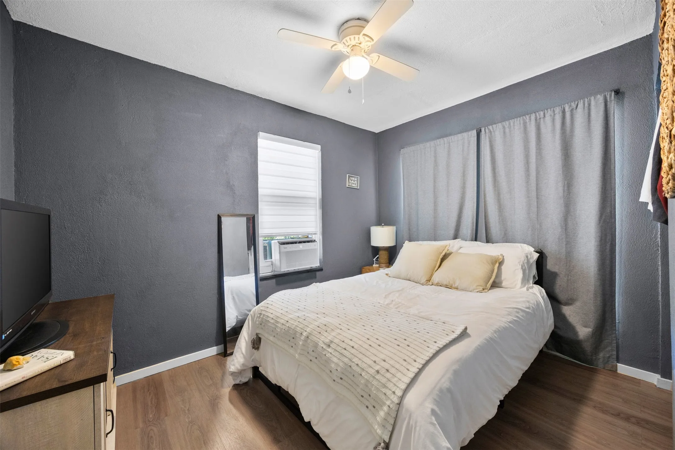 Bedroom featuring wood-finish flooring, a ceiling fan with integrated lighting, and a window with white blinds