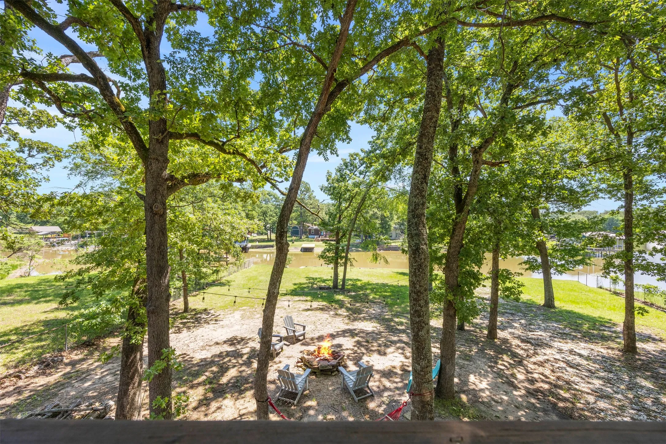 Shaded outdoor area featuring mature trees, string lighting, and a fire pit