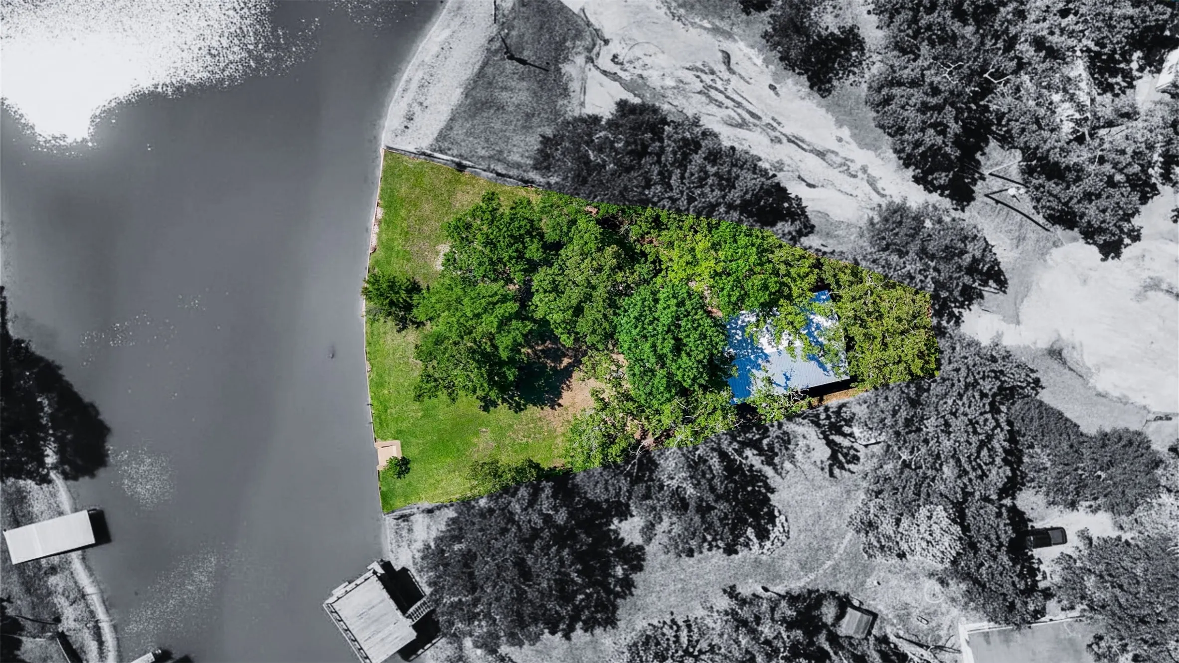 Waterfront property featuring a private boat dock, expansive green lawn, mature trees, and a secluded residence with a blue roof