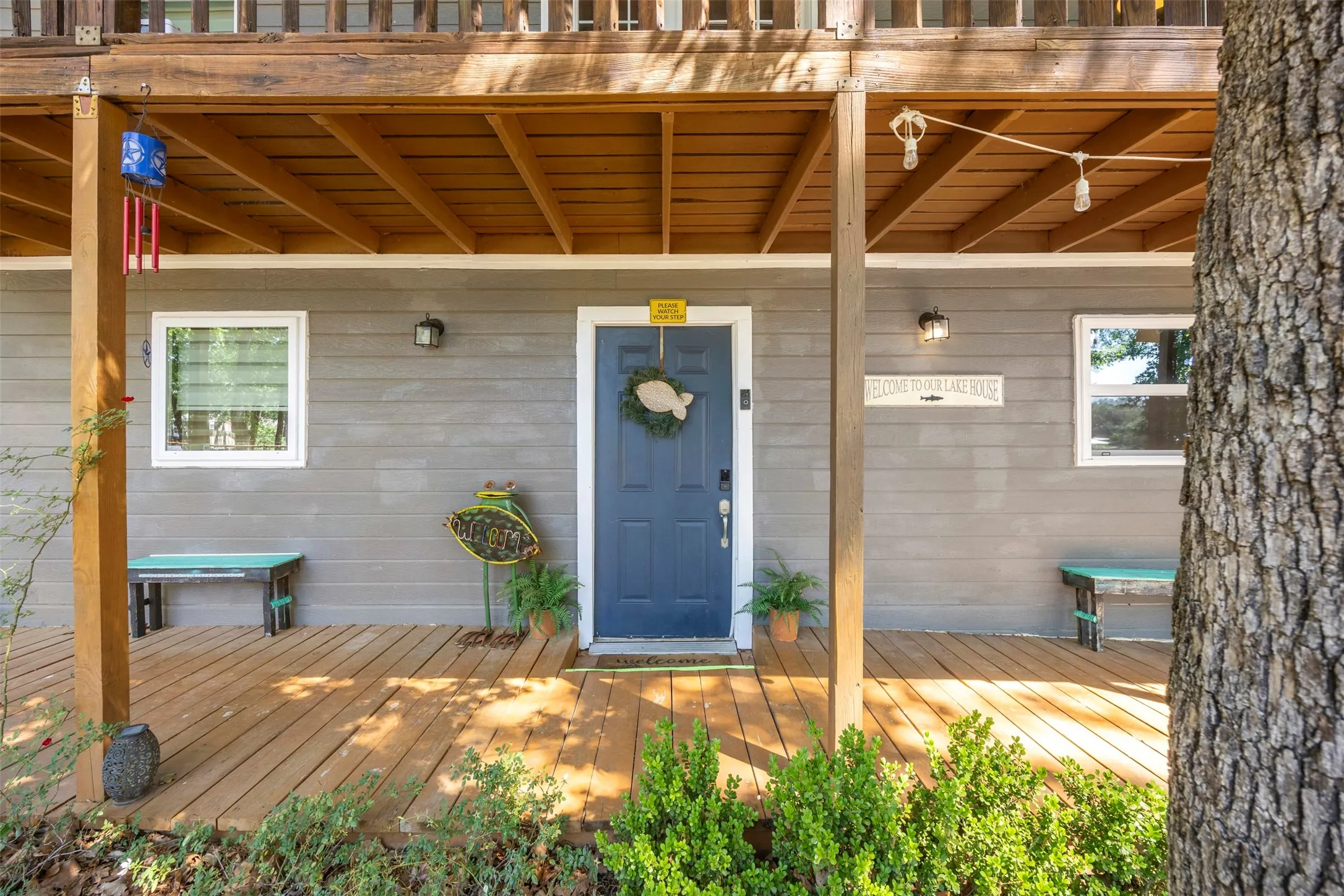 Inviting wooden deck entry featuring a solid blue door with an accent wreath, gray horizontal siding, and white-framed windows