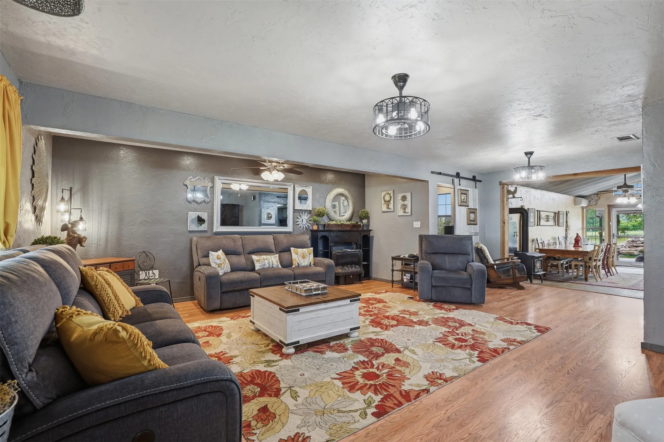 Spacious living area featuring wood-finish flooring, a decorative area rug, and two contemporary ceiling light fixtures