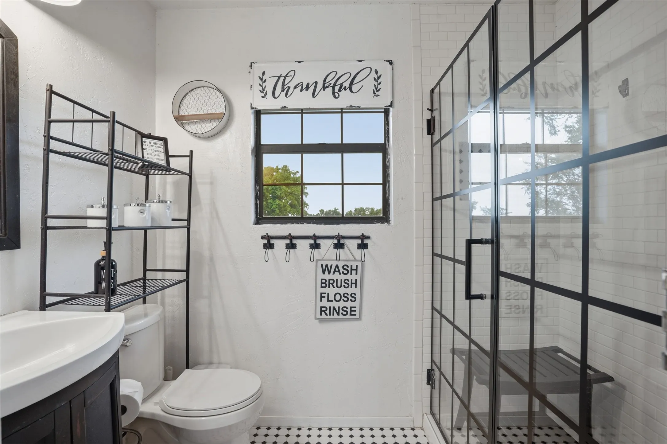 Bathroom featuring a black-framed glass shower enclosure, black-grid window, and black-and-white patterned floor tiling