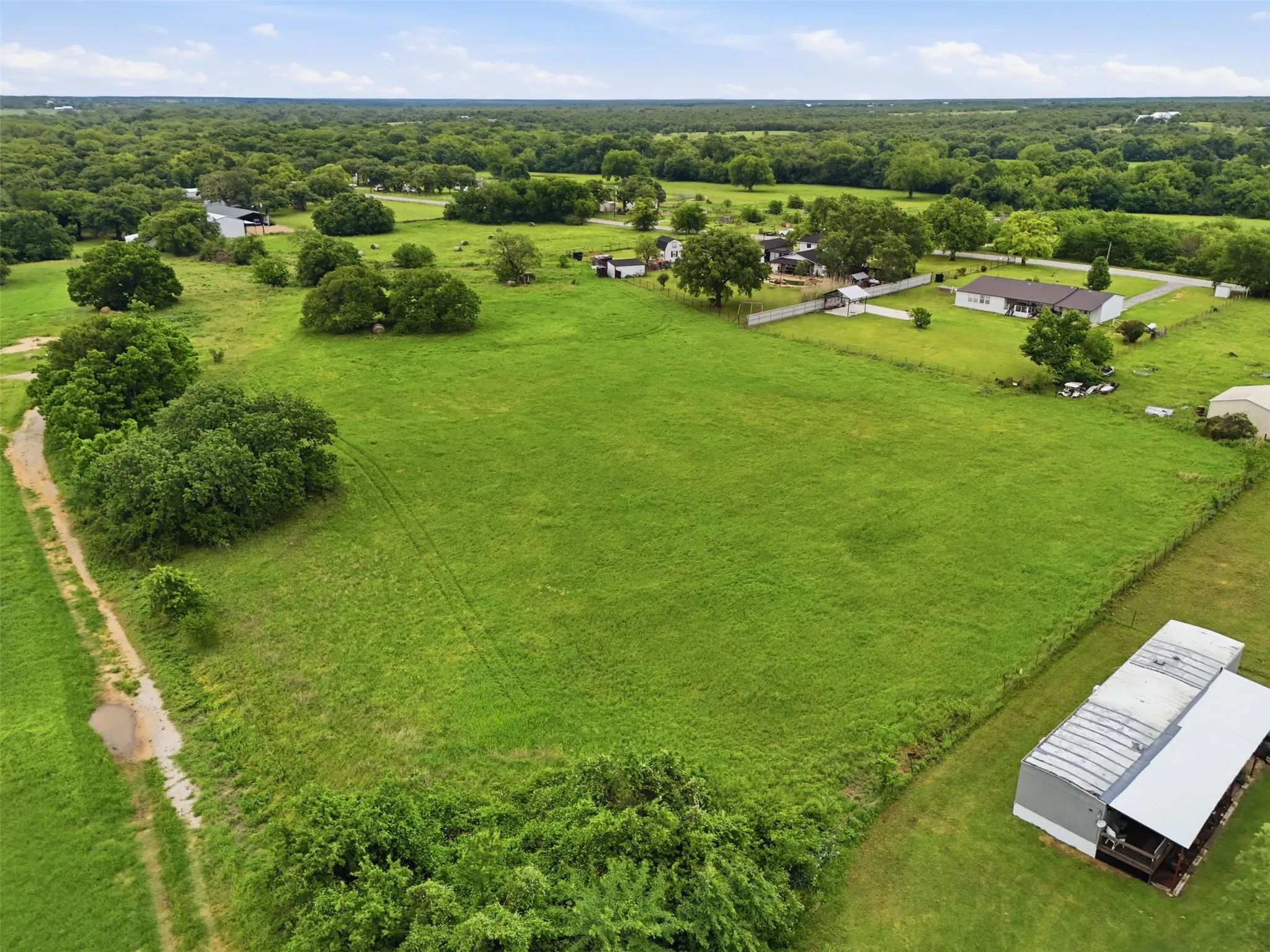 Expansive green field with scattered mature trees and distant residential properties