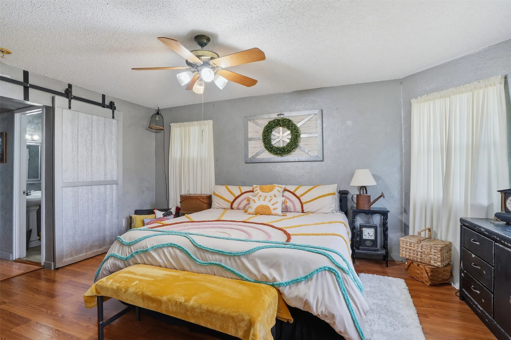 Bedroom featuring wood-finish flooring, a ceiling fan with integrated lighting, and a sliding barn door