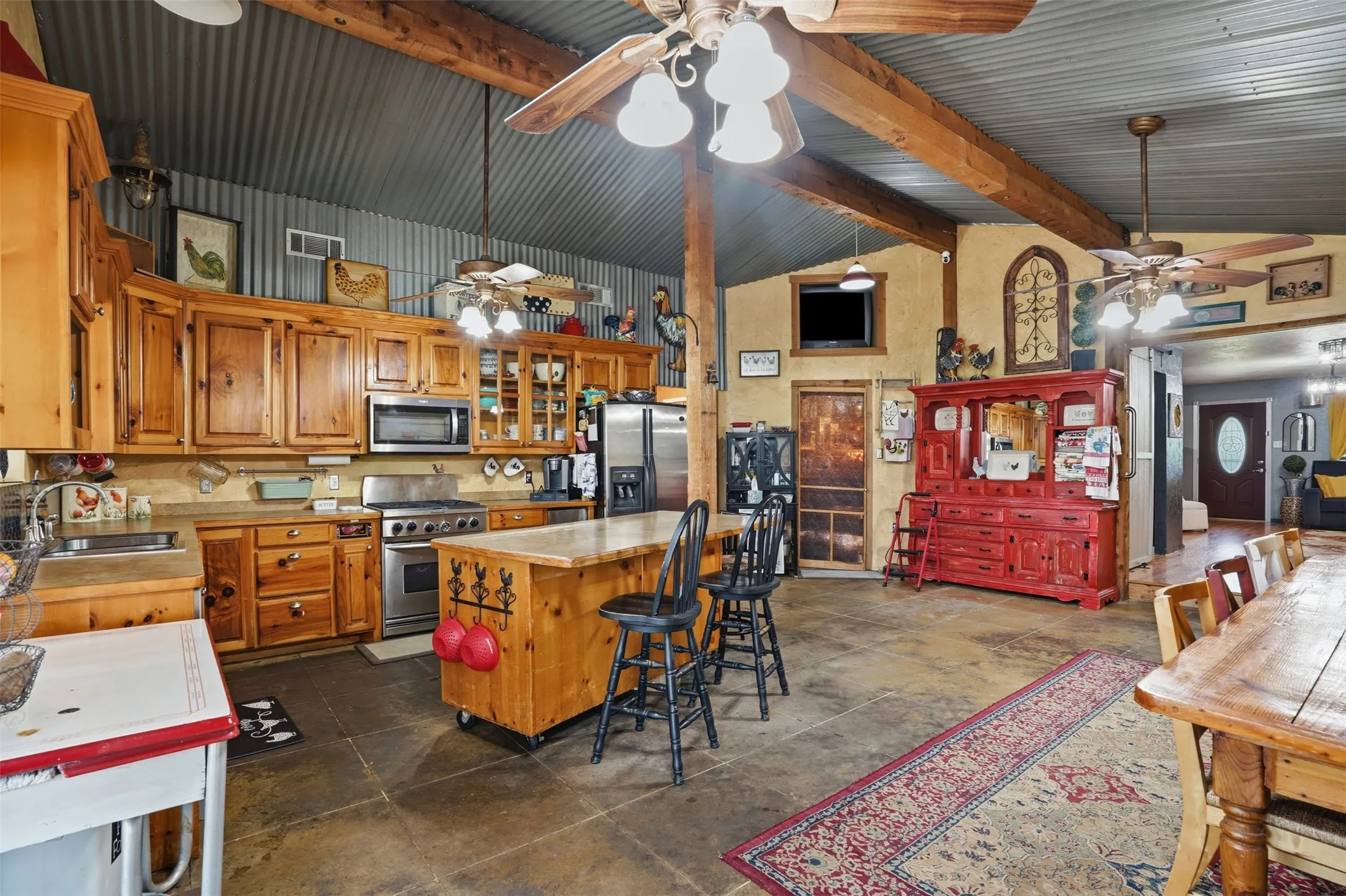 Kitchen featuring wood cabinetry, stainless steel appliances, a central island with bar seating, and a corrugated metal ceiling with exposed wooden beams