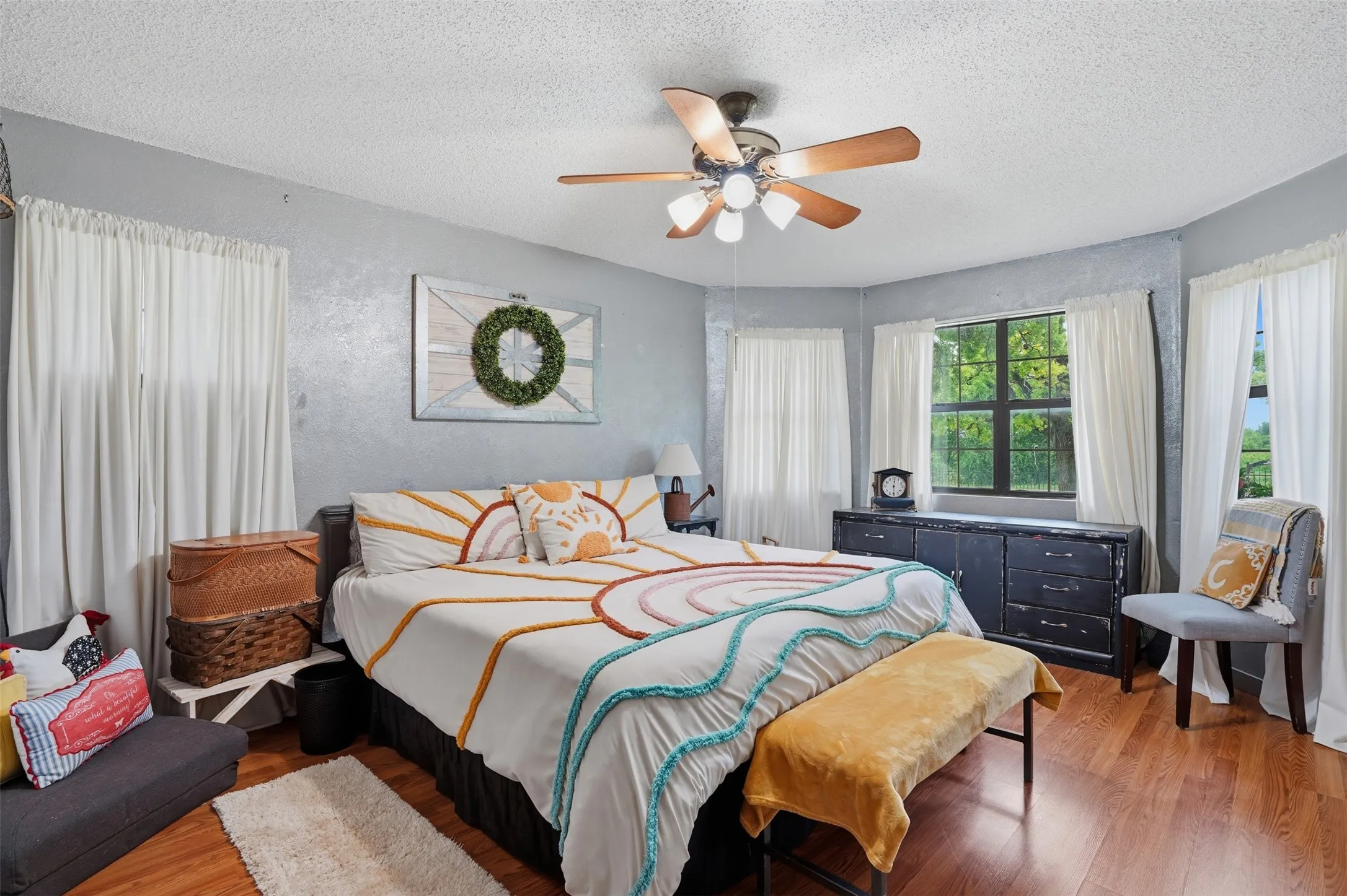Spacious room featuring wood-finish flooring, multiple windows with white curtains, and a ceiling fan with integrated lighting