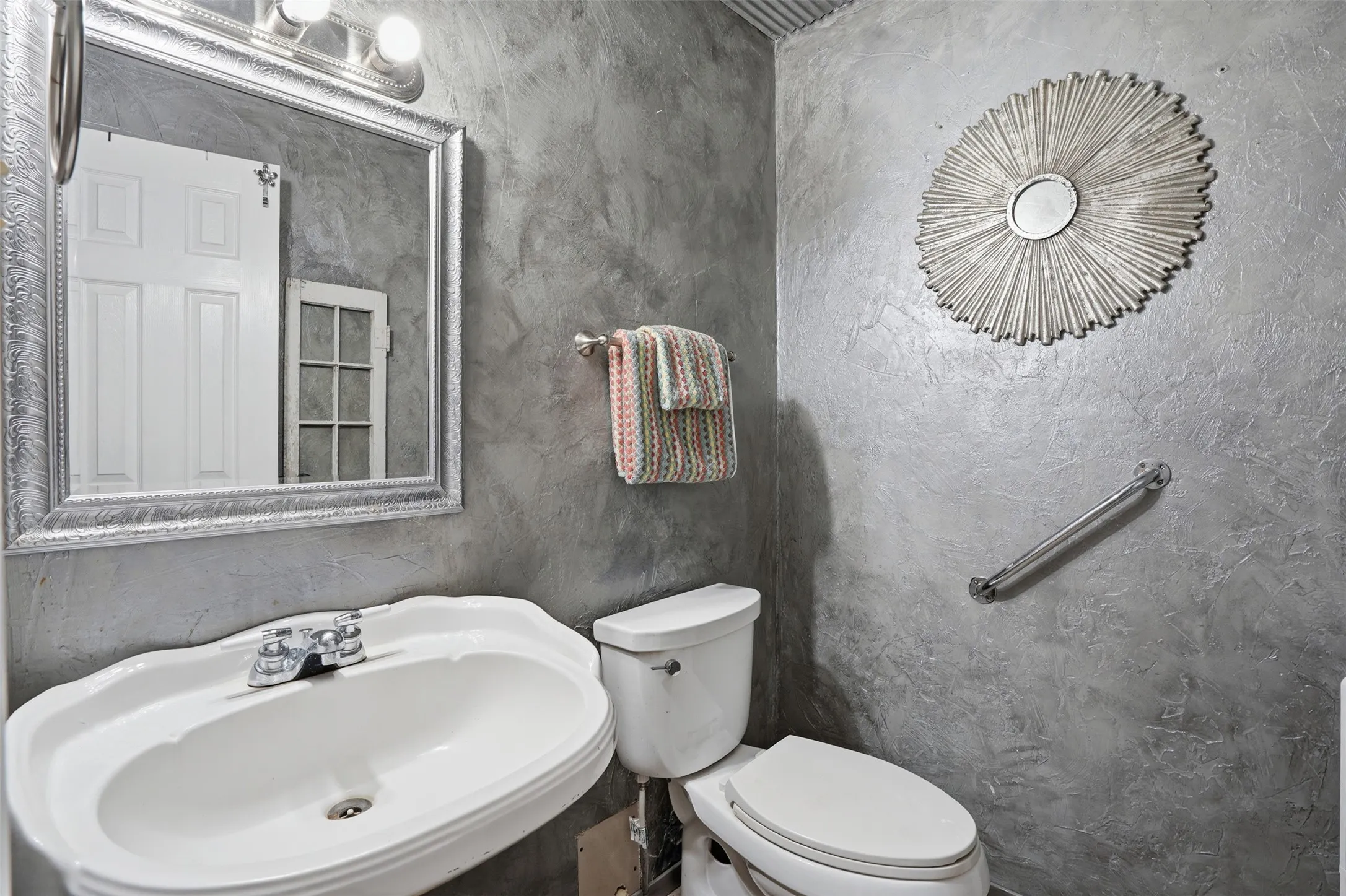 Bathroom featuring textured gray walls, a white pedestal sink, and a framed mirror with integrated lighting