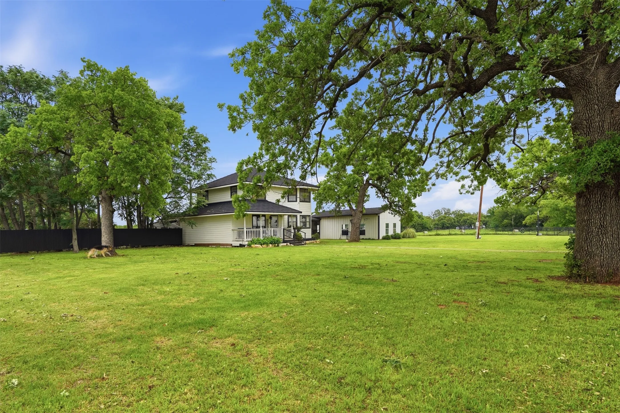 Expansive green lawn with mature trees and a two-story residence featuring a covered porch