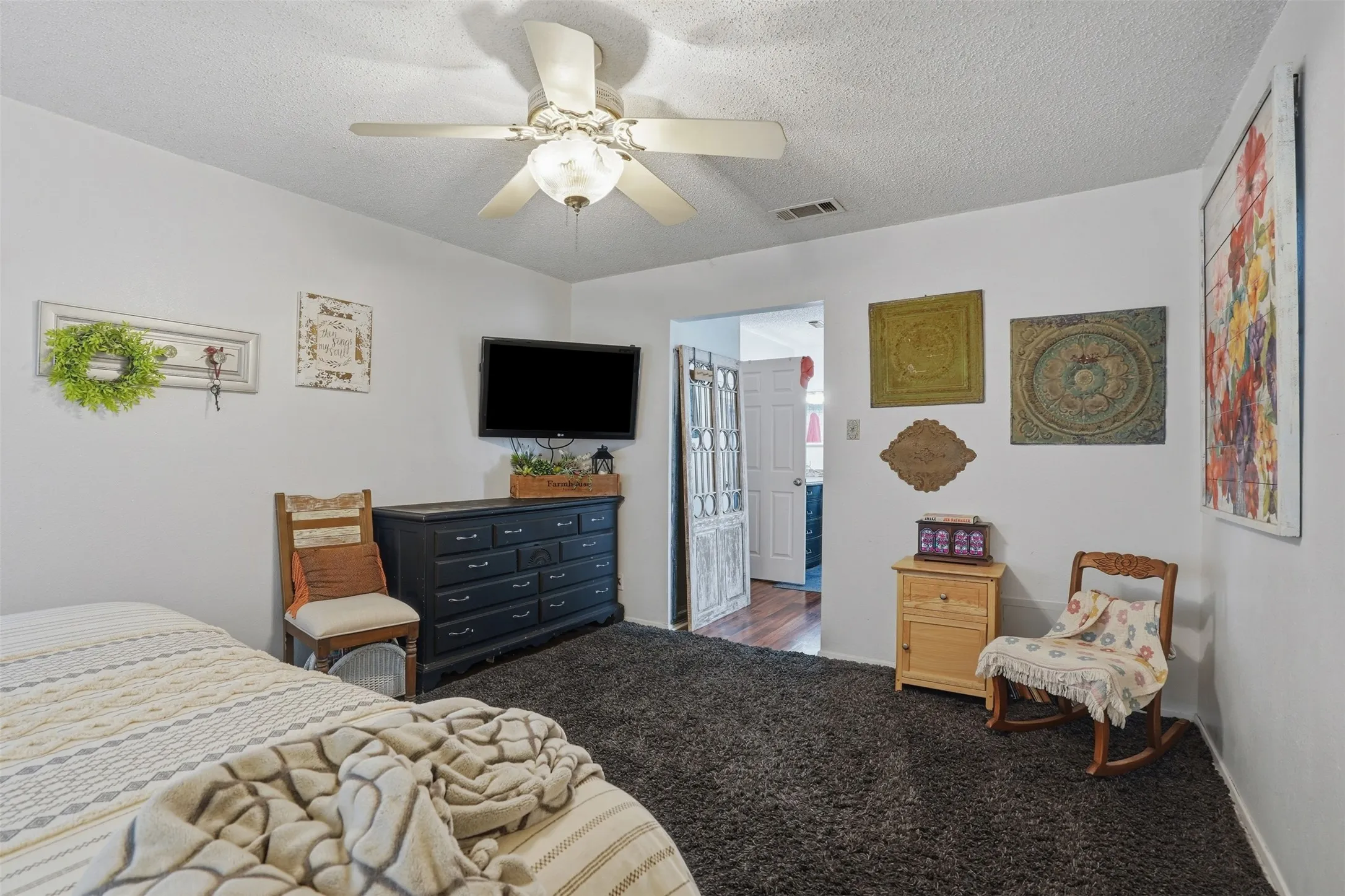 Carpeted room featuring a ceiling fan with integrated lighting, a white painted wall finish, and a doorway with a panel-style door leading to a separate area with wood-finish flooring