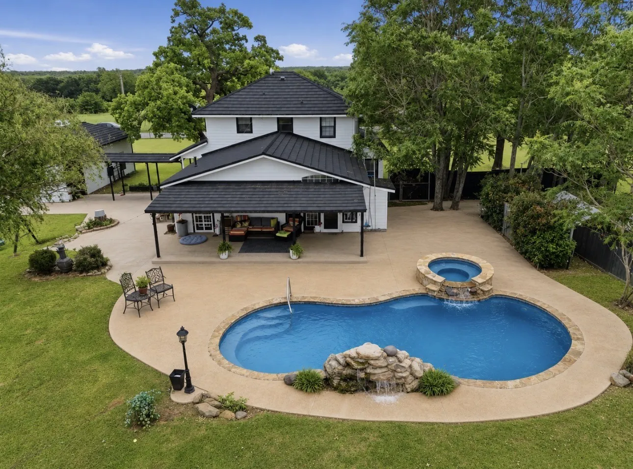 Expansive concrete patio featuring a freeform pool with a rock waterfall and integrated spa