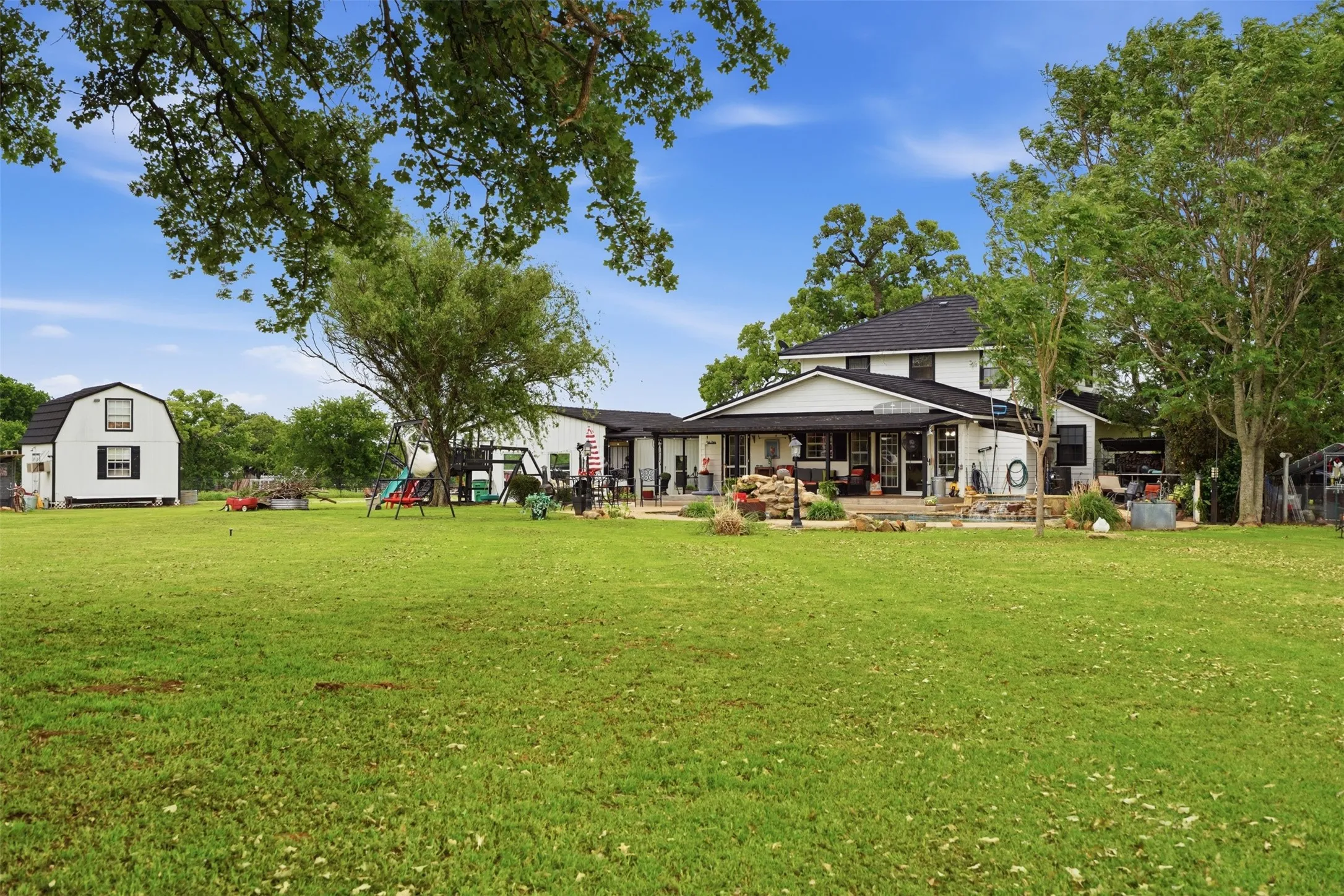 Expansive backyard featuring a large green lawn, mature trees, and a separate gambrel-roofed accessory building