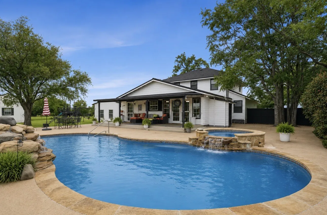 Expansive concrete patio featuring a freeform pool with a rock waterfall and integrated spa