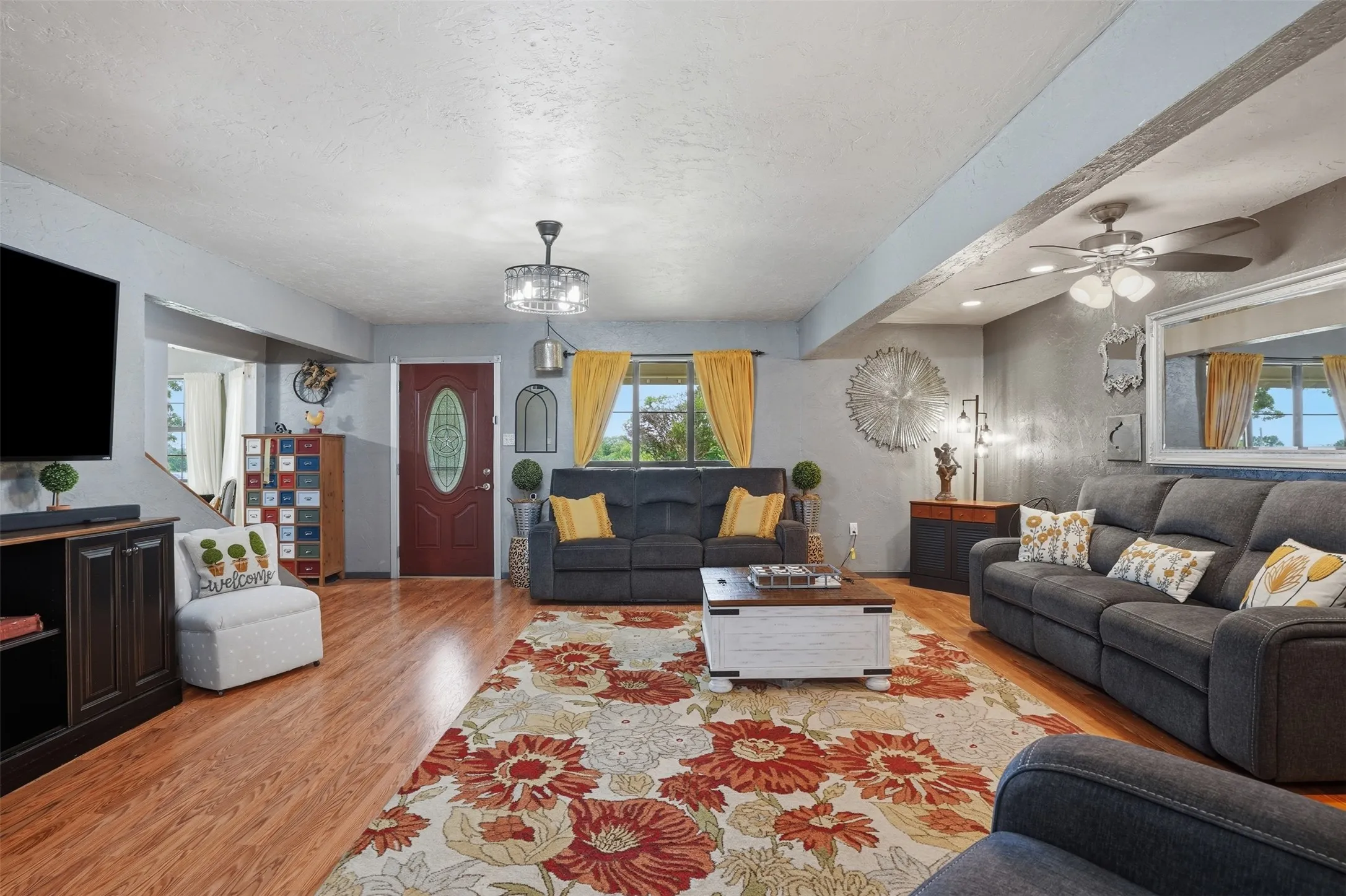 Spacious living area featuring wood-finish flooring, a decorative oval-paneled entry door, and a multi-speed ceiling fan