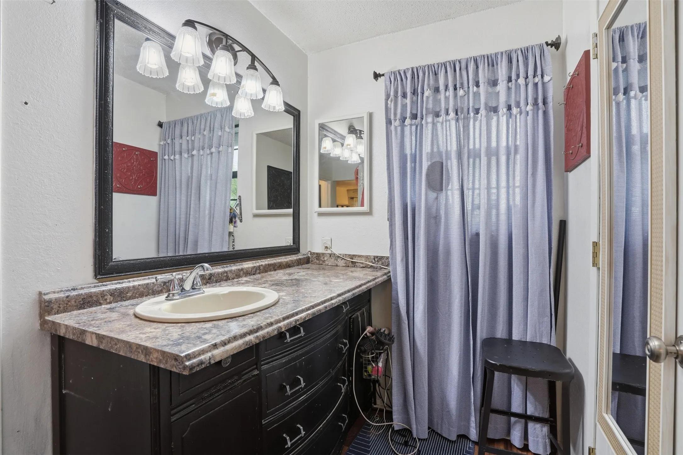 Vanity area featuring a large framed mirror with an arched light fixture, an integrated sink, a patterned countertop, and dark cabinetry