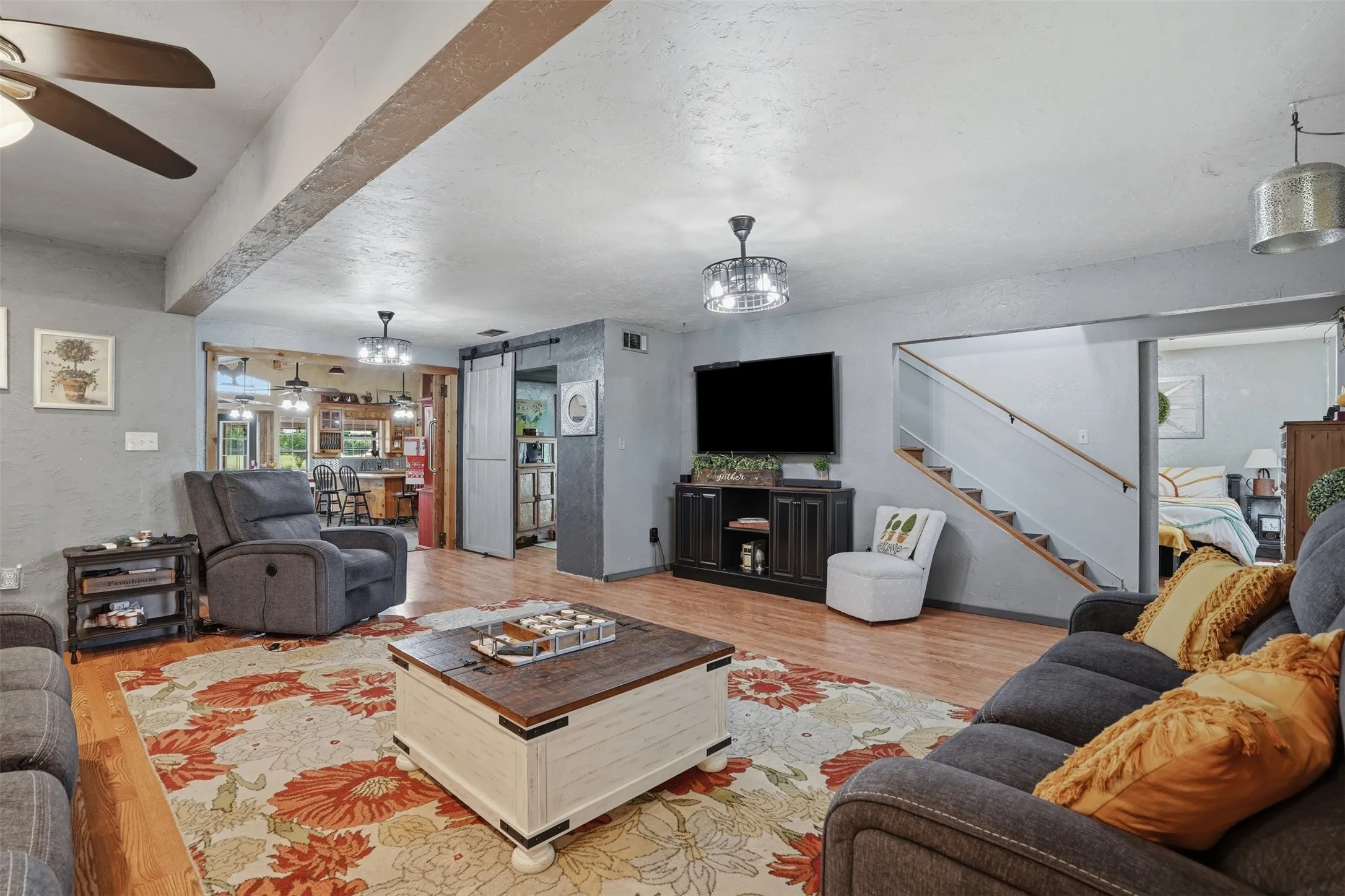 Spacious living area featuring wood-finish flooring, a ceiling fan, and decorative light fixtures