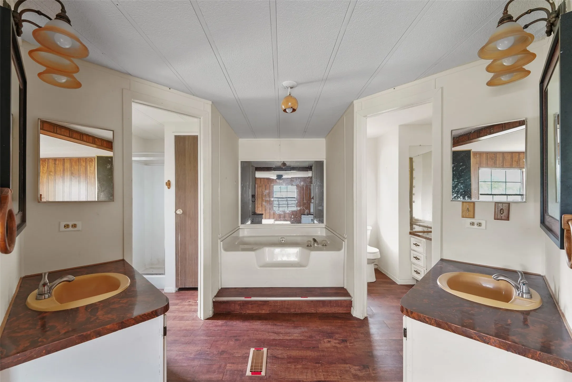 Bathroom featuring a central built-in soaking tub, dual vanity areas with integral sinks and laminate countertops, and wood-finish flooring