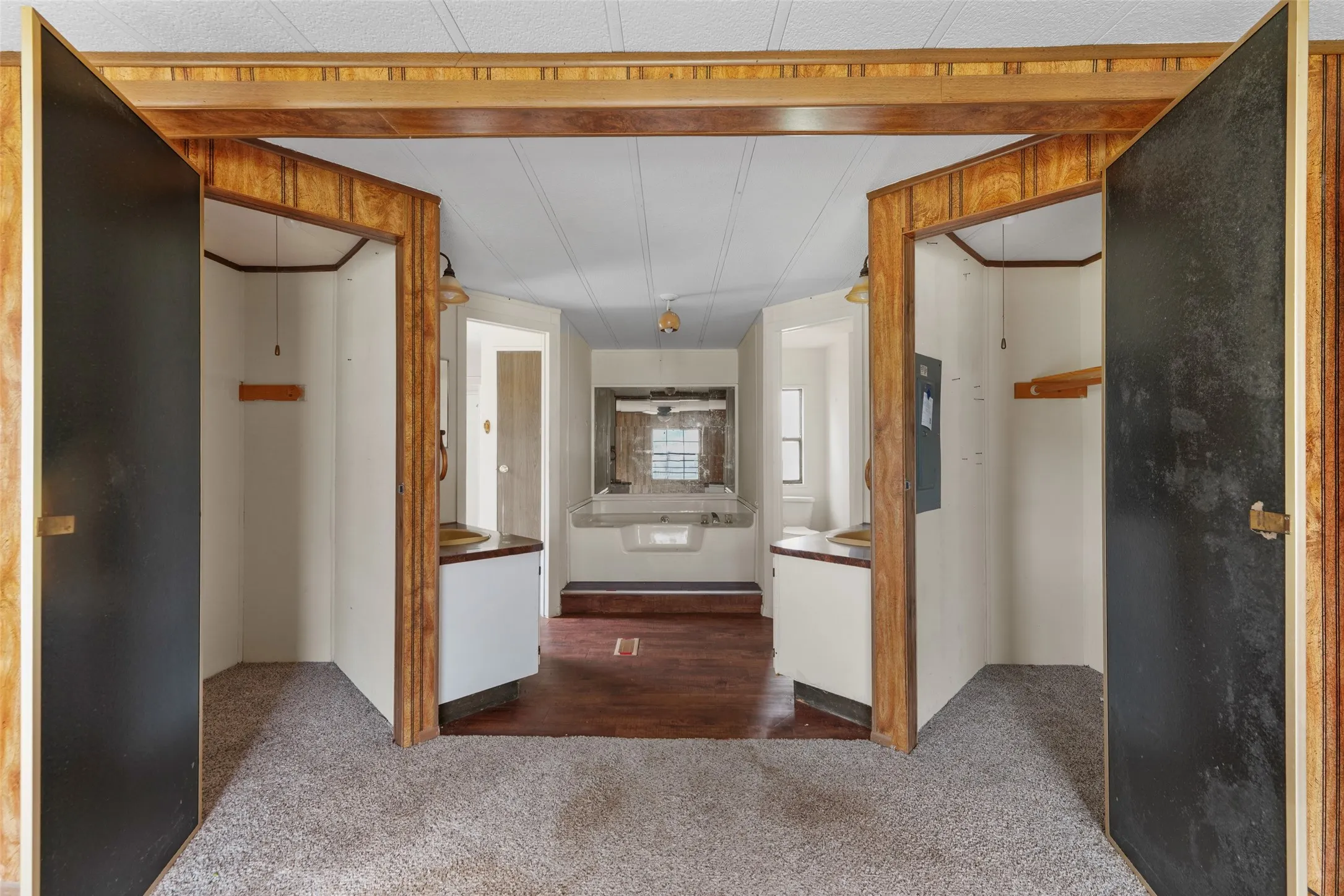 Central room with carpeted flooring leading to two mirrored vanity areas featuring wood-finish paneling and recessed storage