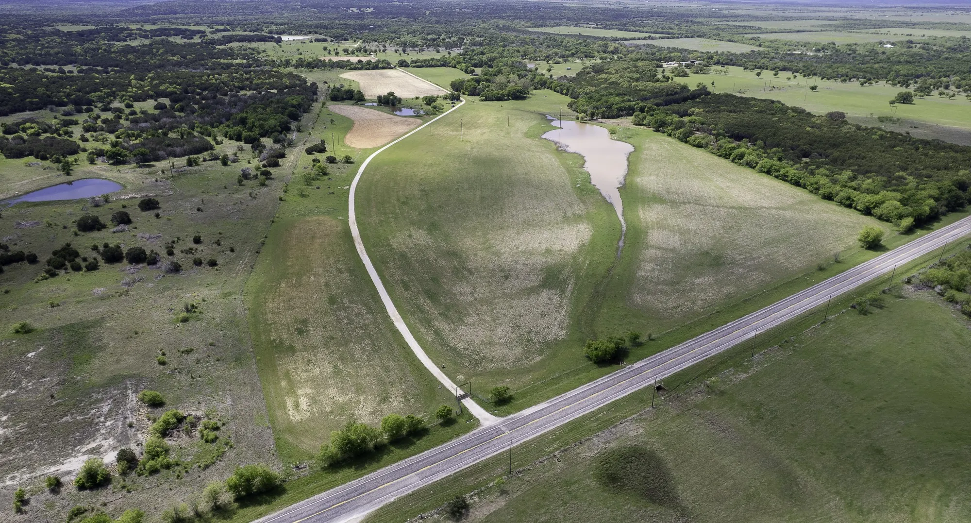 Expansive property featuring varied terrain including open fields, wooded areas, and a road