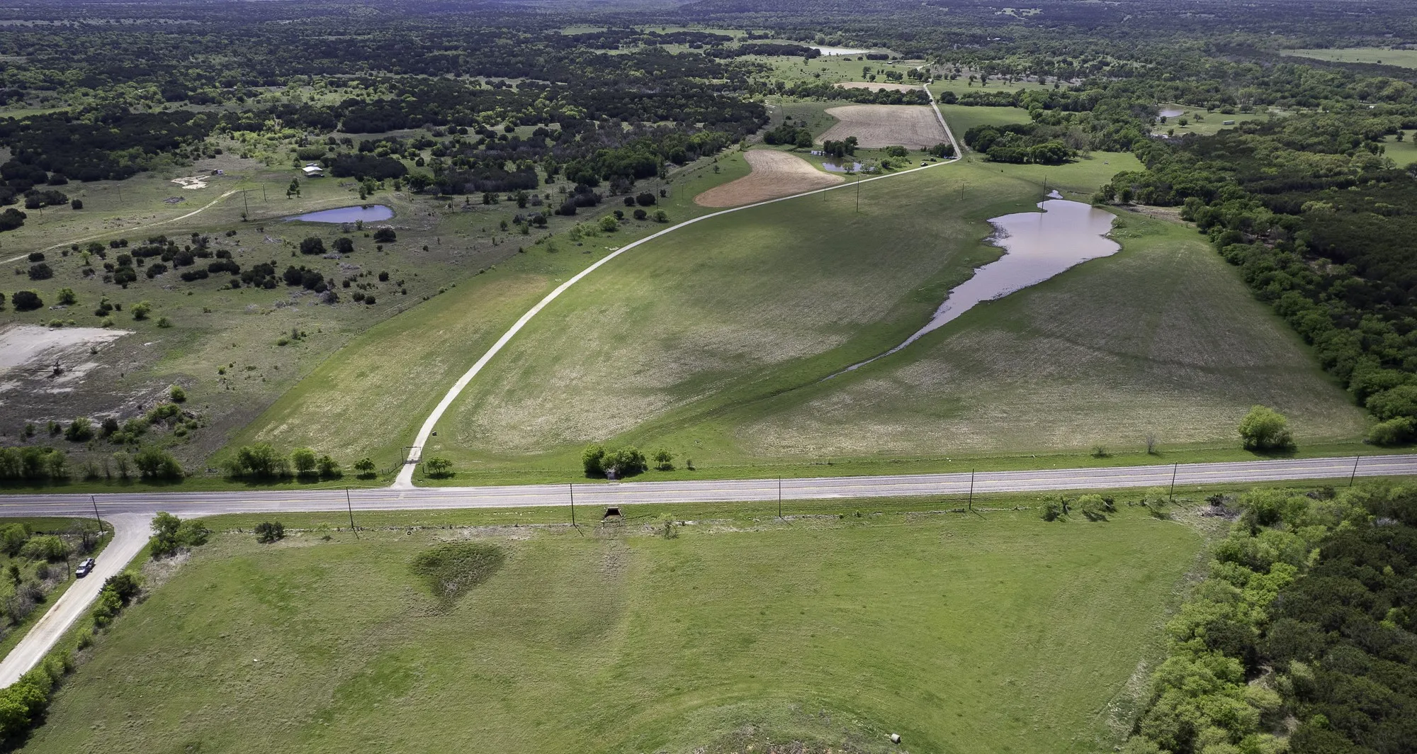 Expansive property featuring a paved road frontage, a pond, and open fields surrounded by trees