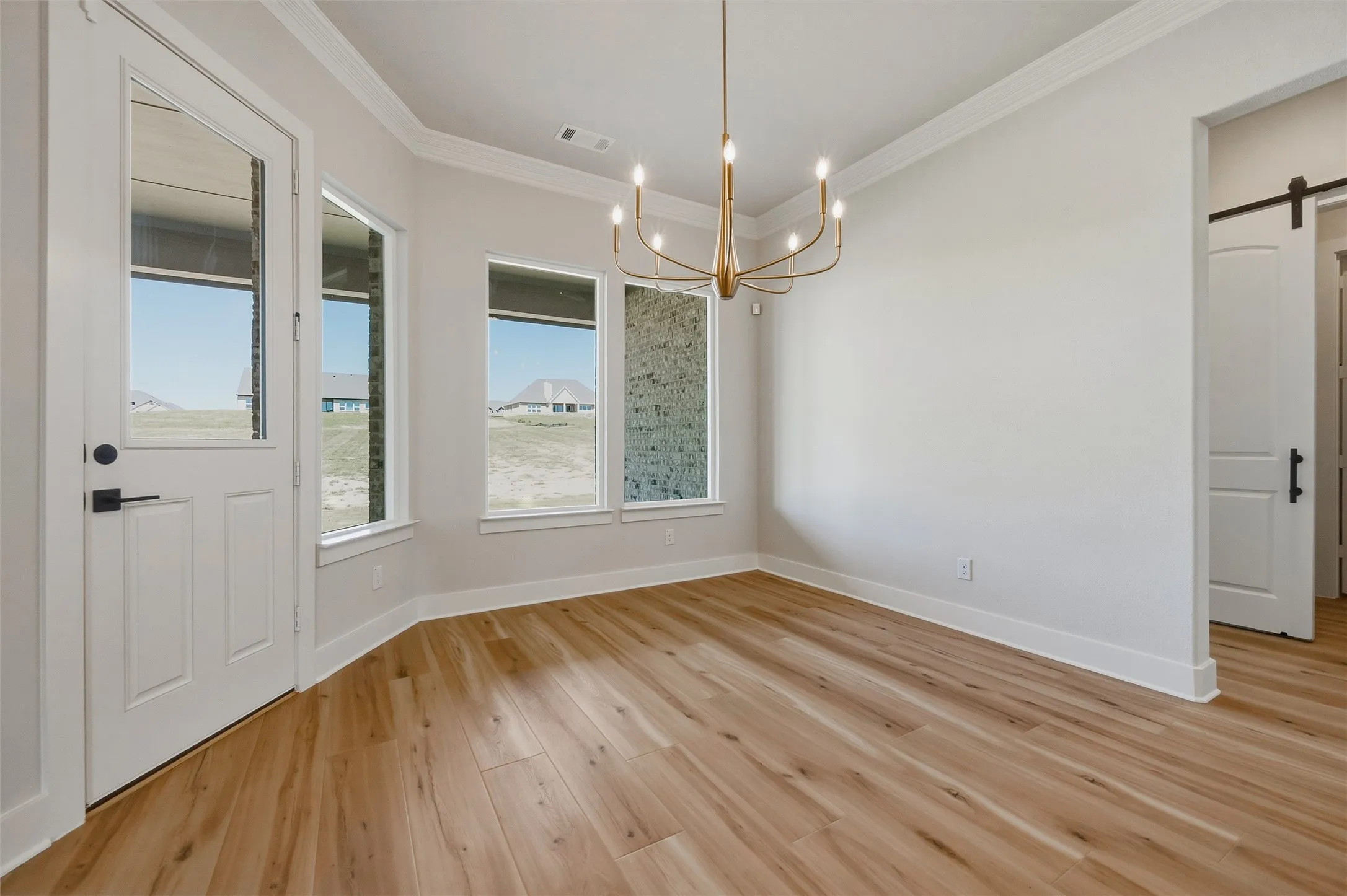 Wood-finish flooring, contemporary chandelier, crisp white trim, and multiple windows providing natural light