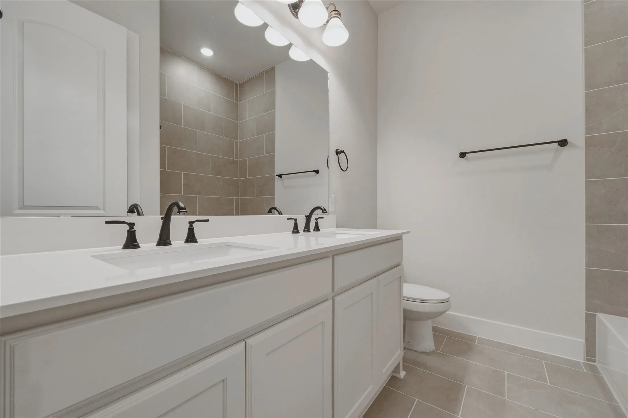Double vanity with integrated sinks and black fixtures, white cabinetry, light countertop, and tiled flooring