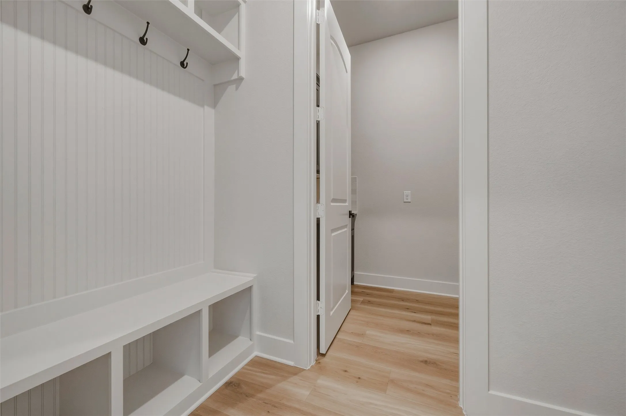 Built-in bench with cubby storage, beadboard wall paneling, and wood-finish flooring