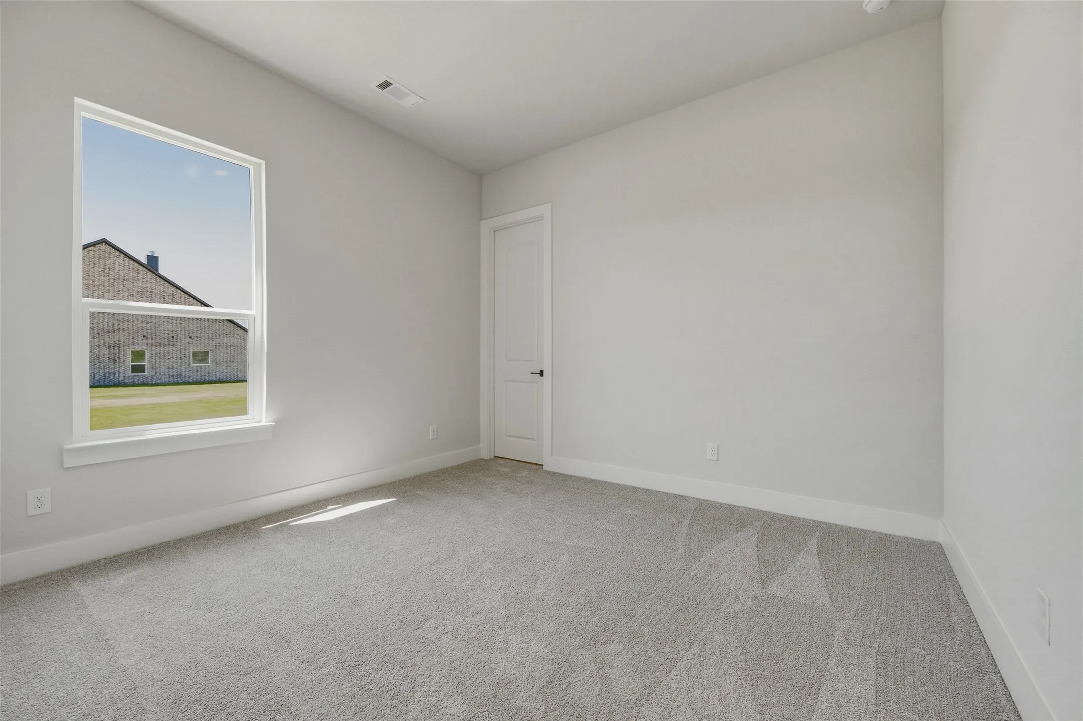 Light gray wall paint, white trim, single-pane window, light gray carpet, and a white interior door with black hardware
