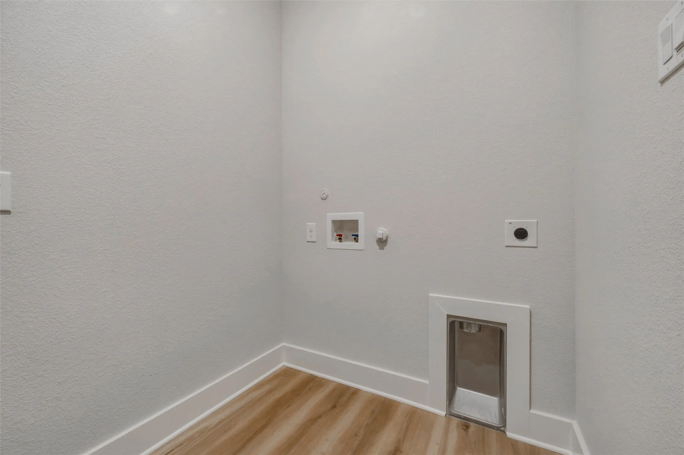 Dedicated laundry area featuring wood-finish flooring, white walls, and a built-in dryer vent