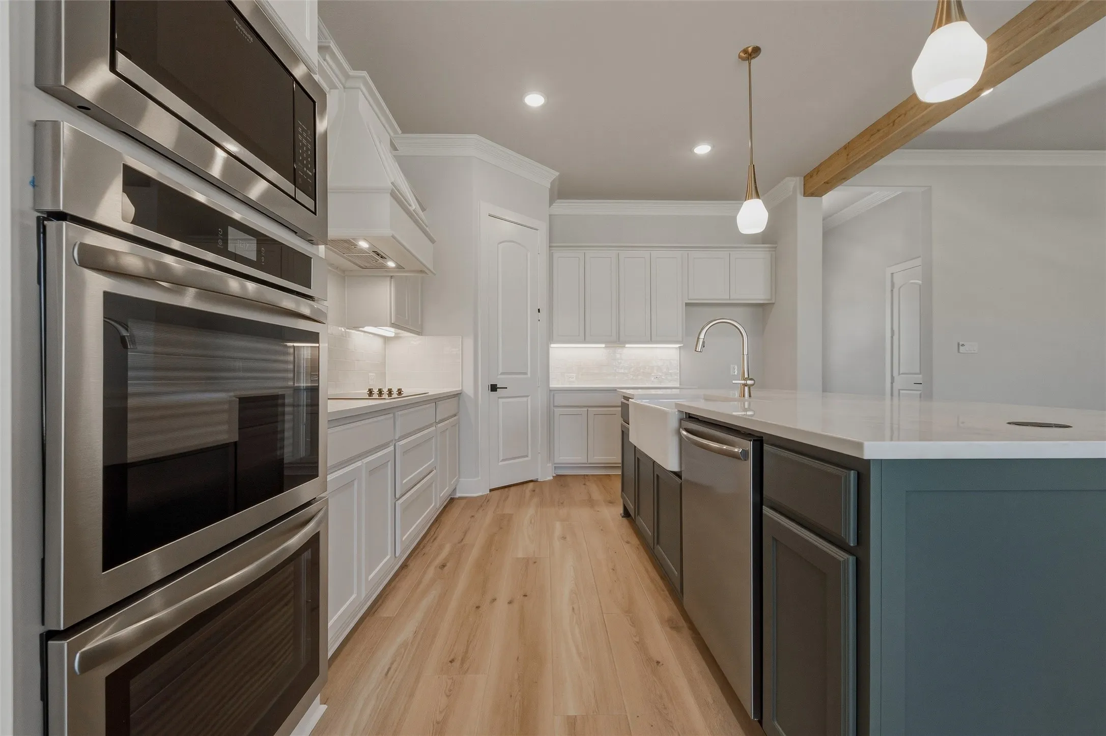 Gourmet kitchen featuring stainless steel appliances, wood-finish flooring, white cabinetry, a large kitchen island with a farmhouse sink, and pendant lighting