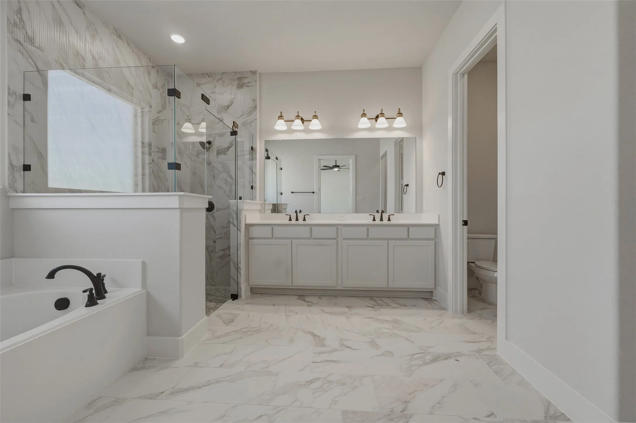 White marble-look flooring, dual vanity with undermount sinks, frameless glass shower enclosure, built-in soaking tub with dark-finish fixtures, and a marble-look shower surround